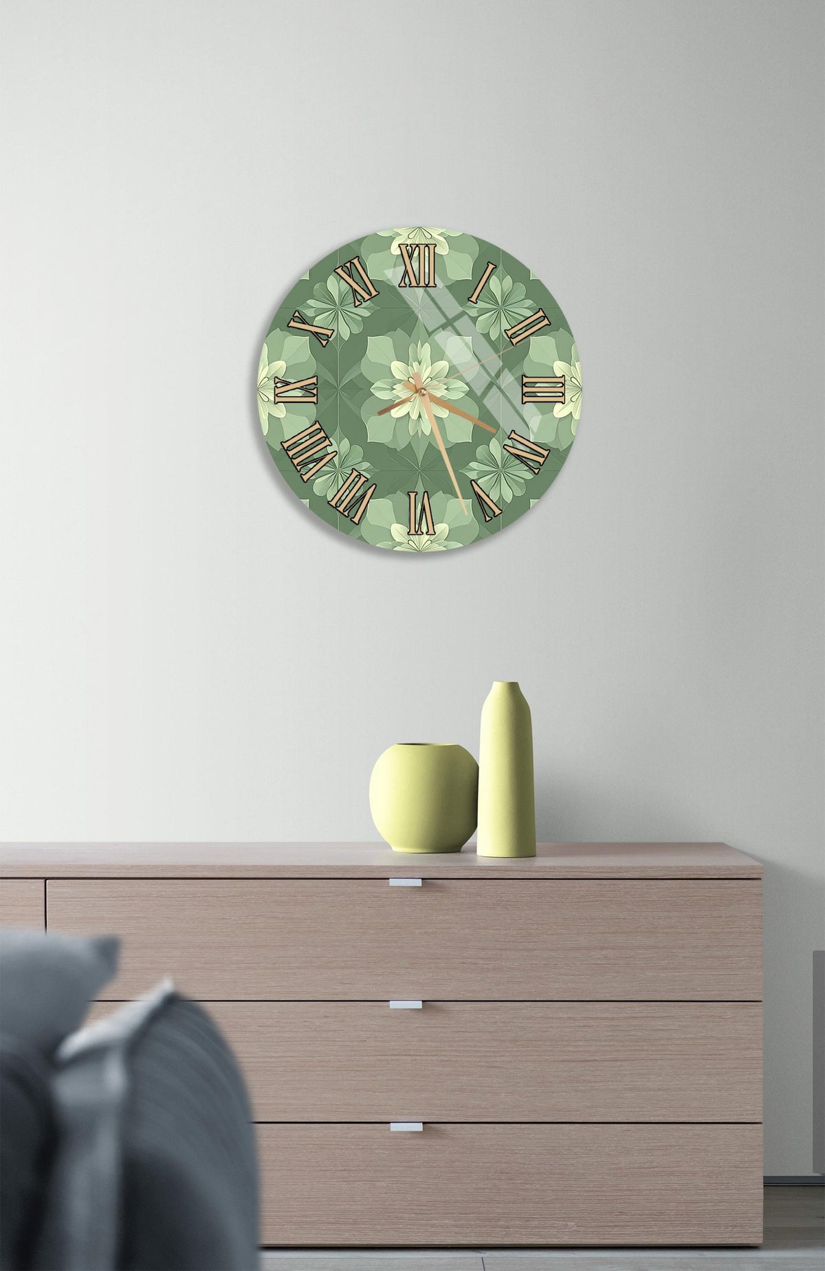 a wall clock with a green floral design, mounted on a wall above a wooden dresser with three drawers.