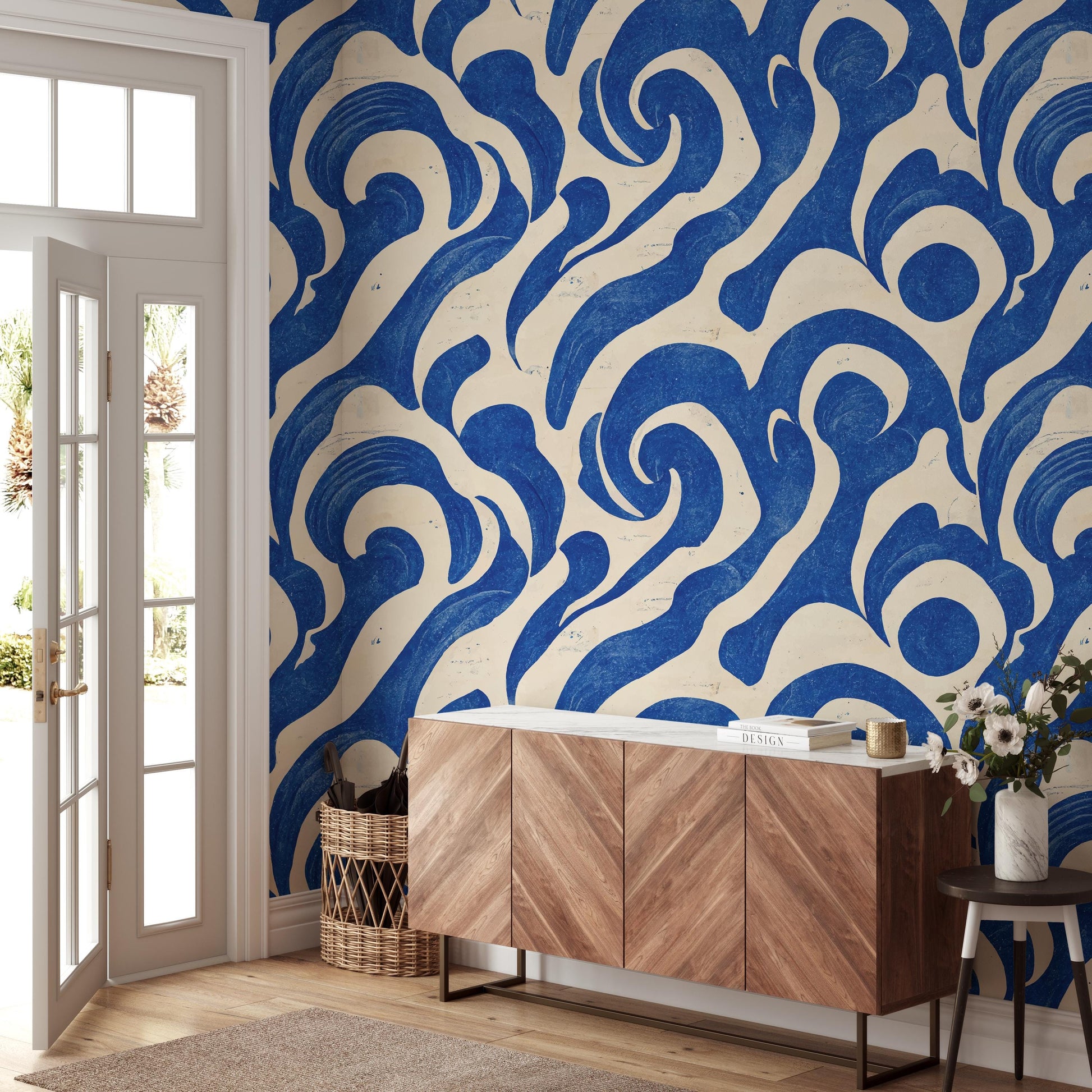 a room with a large blue and white abstract pattern on the wall, a wooden cabinet or sideboard, and a small table with a vase of flowers.