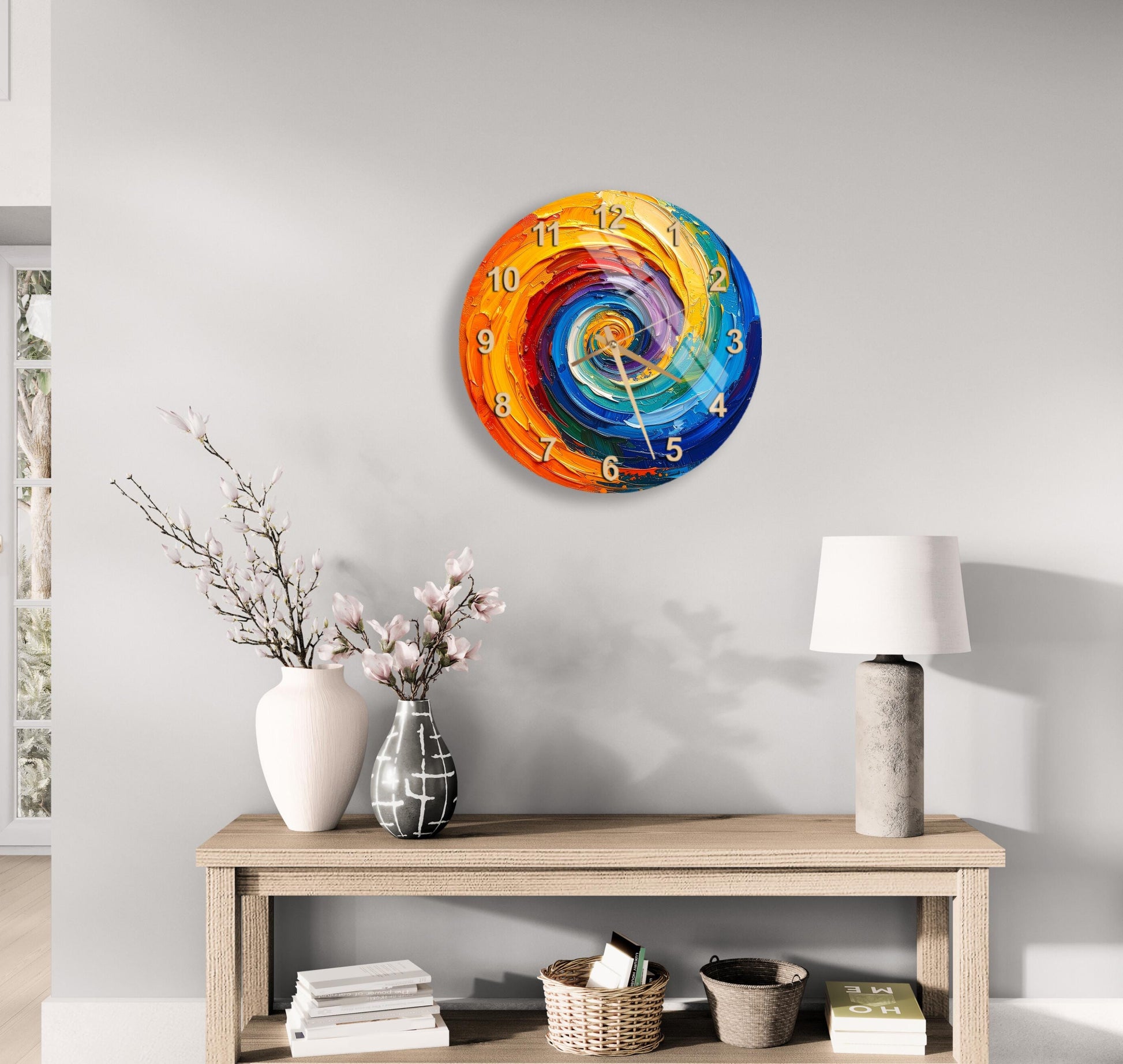 a modern, colorful clock with a spiral design on a wall above a wooden table with a lamp, a vase with flowers, and some books.