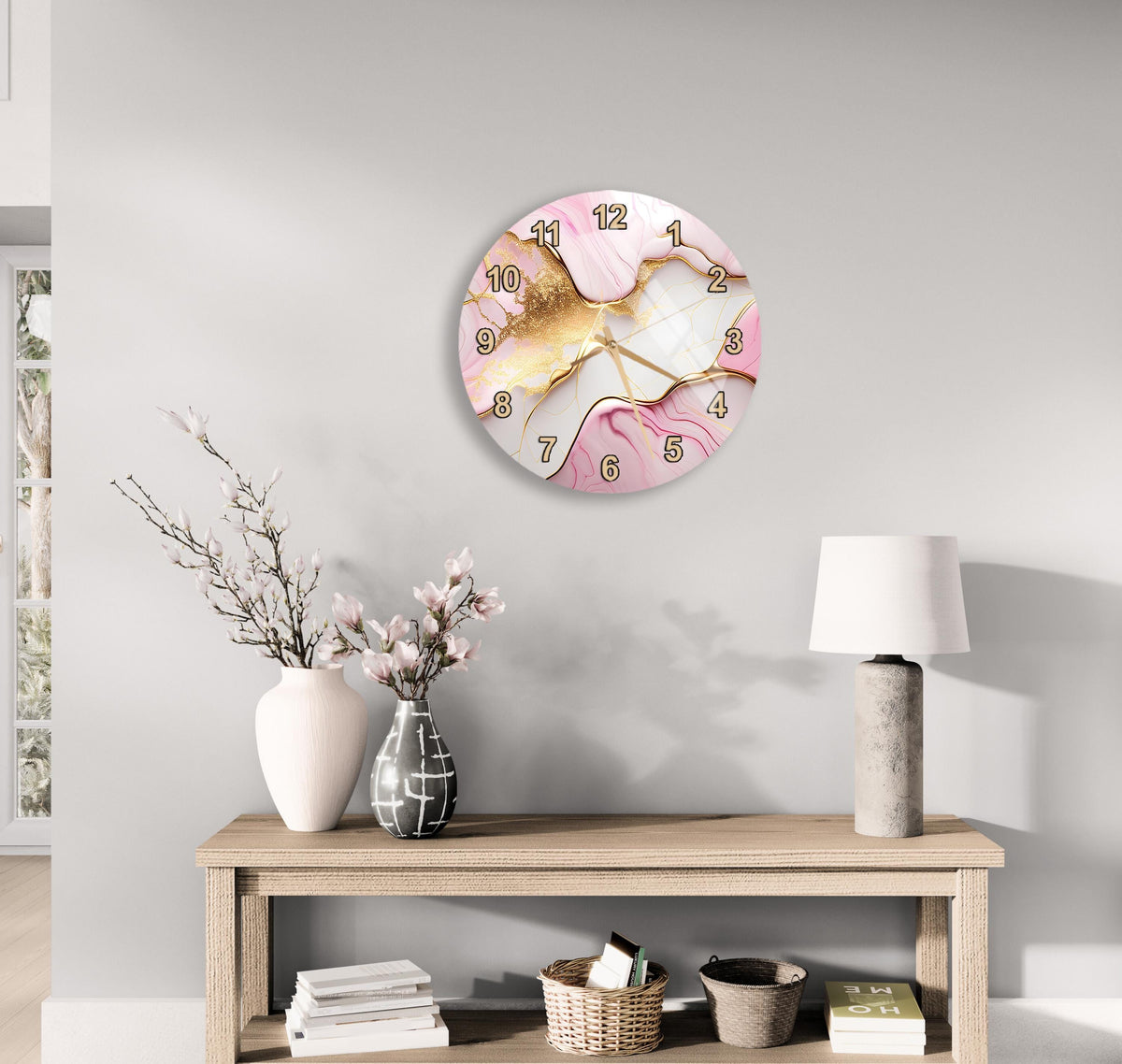a wall clock with a pink and gold marble design, a wooden table with a lamp, a vase with flowers, and some books on a shelf.