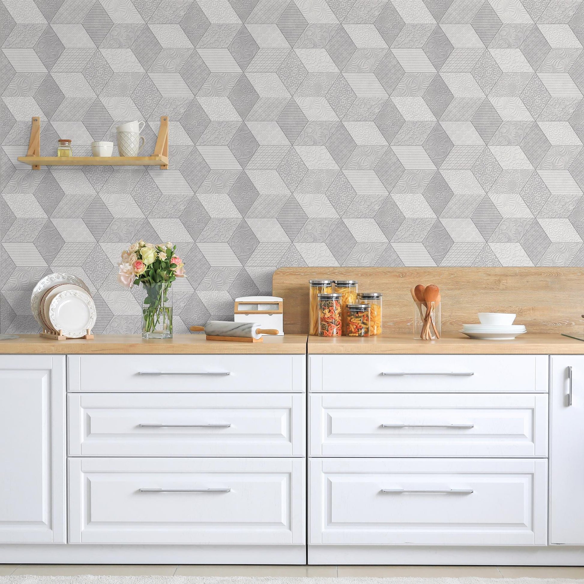 a modern kitchen with a white countertop and drawers, complemented by a geometric patterned wallpaper. On the countertop, there are various kitchen items such as a vase with flowers, a stack of books, and a bowl. The overall scene conveys a clean and organized kitchen design.