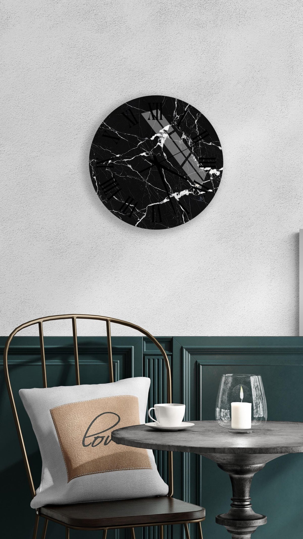 a black marble clock with a white face, mounted on a wall above a table with a white tablecloth and a candle.