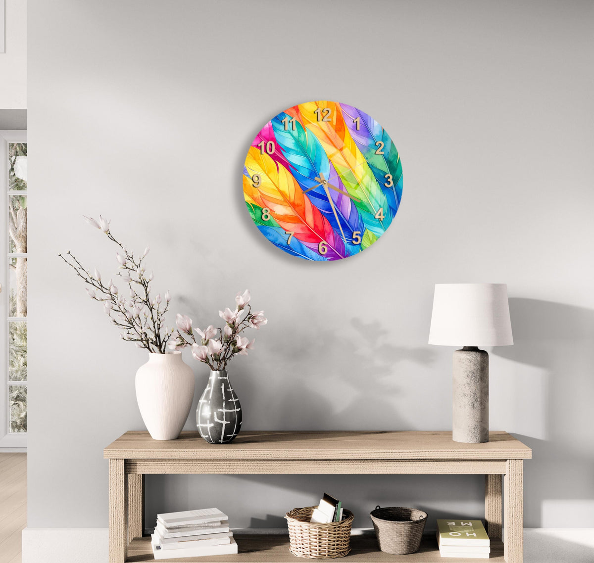 a wall clock with a vibrant feather design, a wooden table with a lamp, a vase with flowers, and a stack of books.