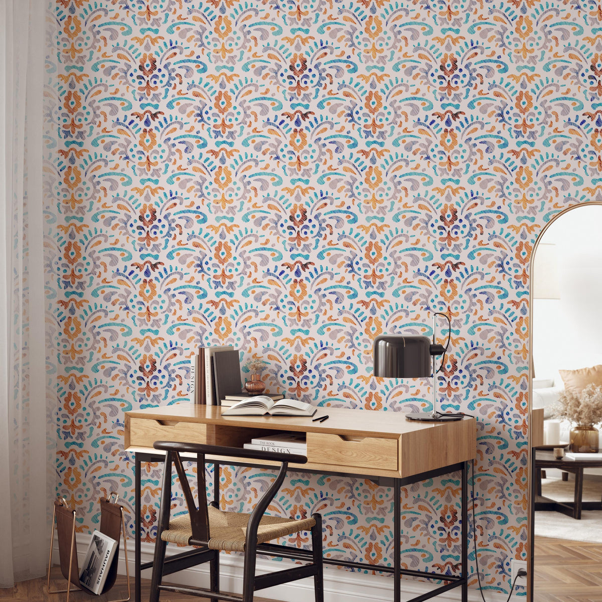 a modern and stylish workspace with a wooden desk, a black chair, and a lamp. The desk is positioned against a wall with a colorful, patterned wallpaper. There are several books and decorative items on the desk, suggesting a well-organized and functional workspace.
