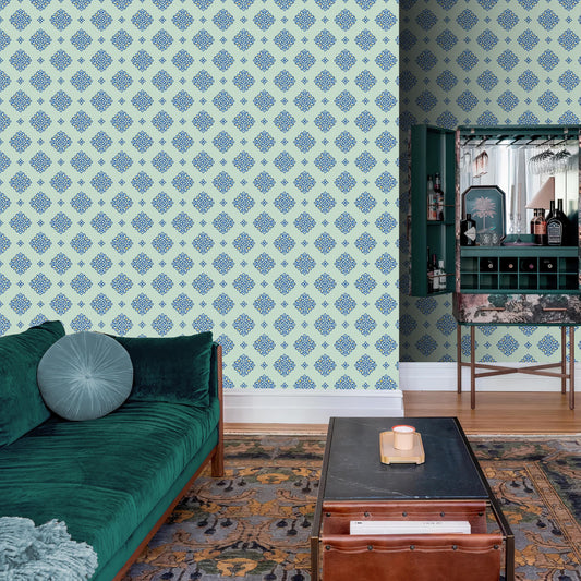 a living room with a green sofa, a wooden coffee table, and a patterned rug. The walls are adorned with a blue and white patterned wallpaper, and there is a bar cabinet with a mirror and shelves filled with various bottles and glasses.