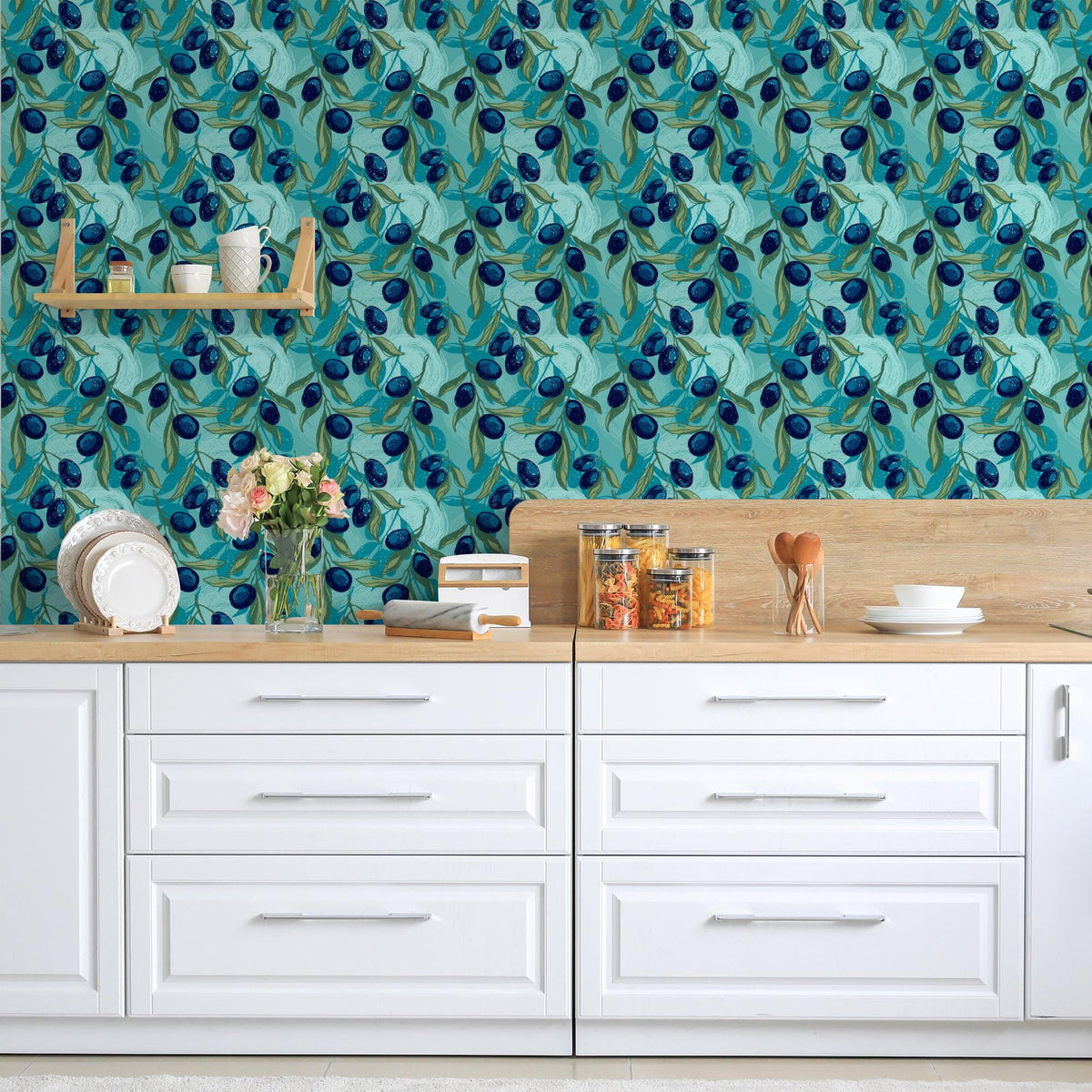 a kitchen counter with various items on it, including a vase of flowers, a stack of books, and a bowl. The counter is set against a wall with a blue and green floral wallpaper.