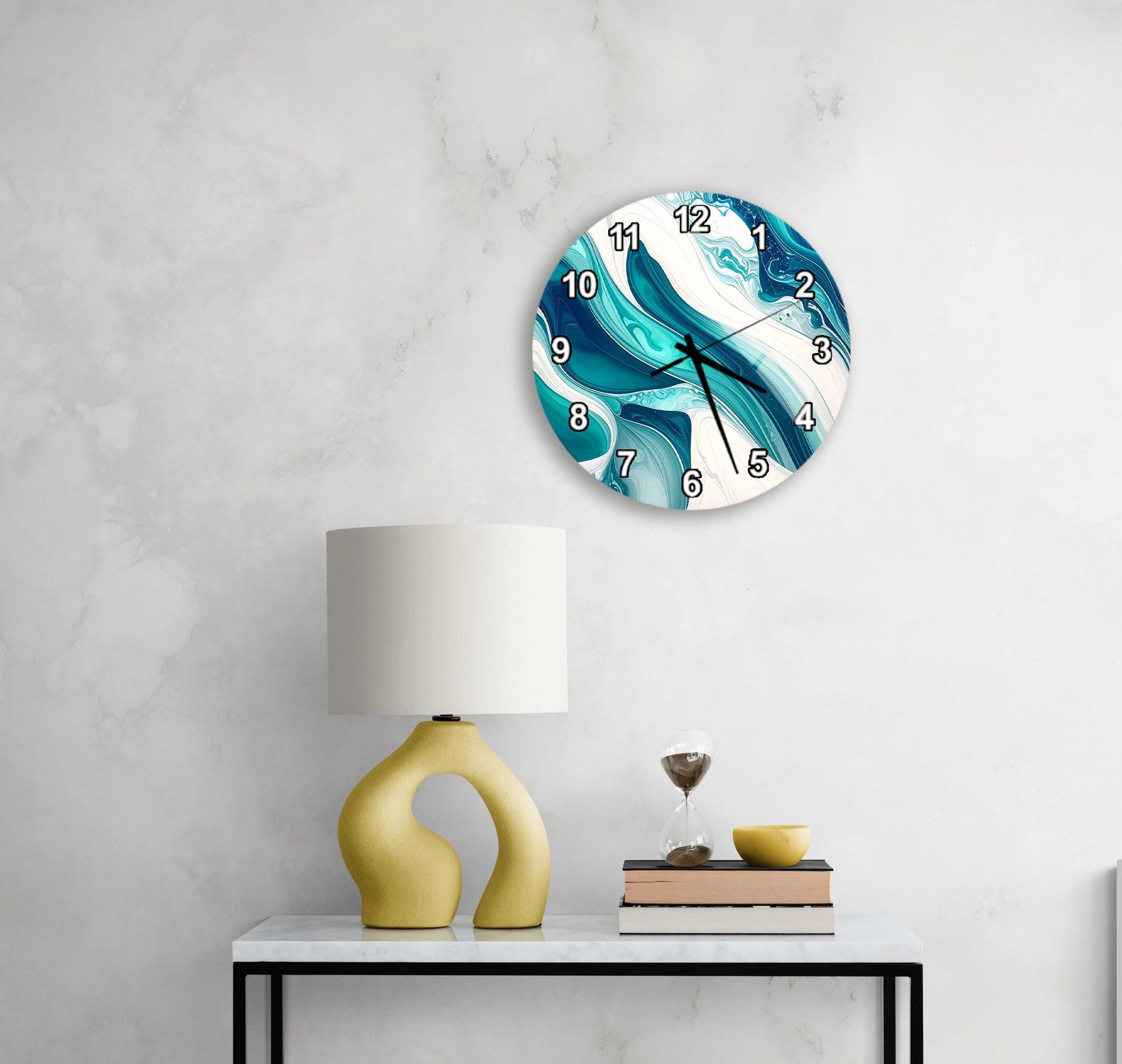 a modern, abstract-style clock with a blue and white swirl design, mounted on a wall above a white table with a yellow lamp and a stack of books.