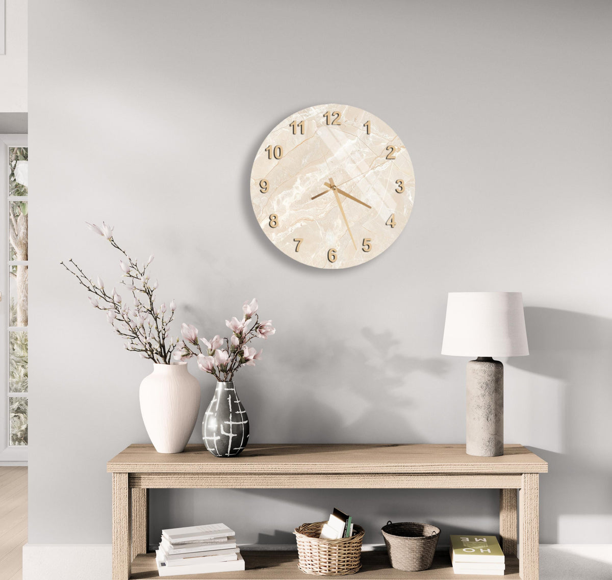 a minimalist living room with a round wall clock, a wooden table with a lamp, a vase with flowers, and a stack of books.