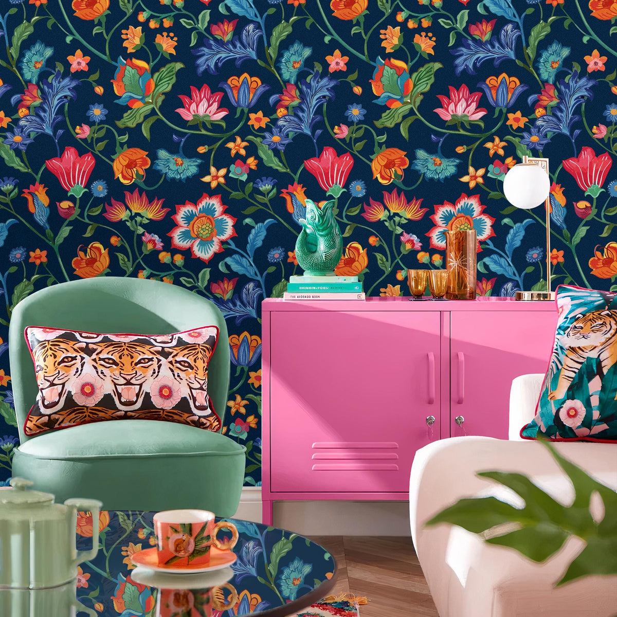 a vibrant and eclectic living room with a bold floral wallpaper, a pink cabinet, a green armchair, a glass coffee table, and various decorative elements such as a vase, a lamp, and a plant.