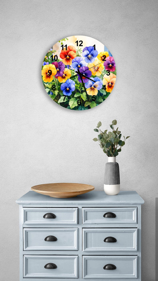 a round wall clock with a vibrant floral design, mounted on a wall above a light blue dresser with six drawers. The clock has a white face with black numbers and hands, and the floral design includes various colors and types of flowers. A small vase with greenery is placed on the dresser, and a wooden bowl is also present on the dresser.