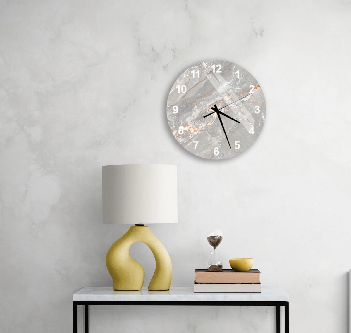 a modern living room with a white marble wall, a round clock with a marble design, a yellow lamp with a unique curved base, a stack of books, and a glass of wine on a white table.