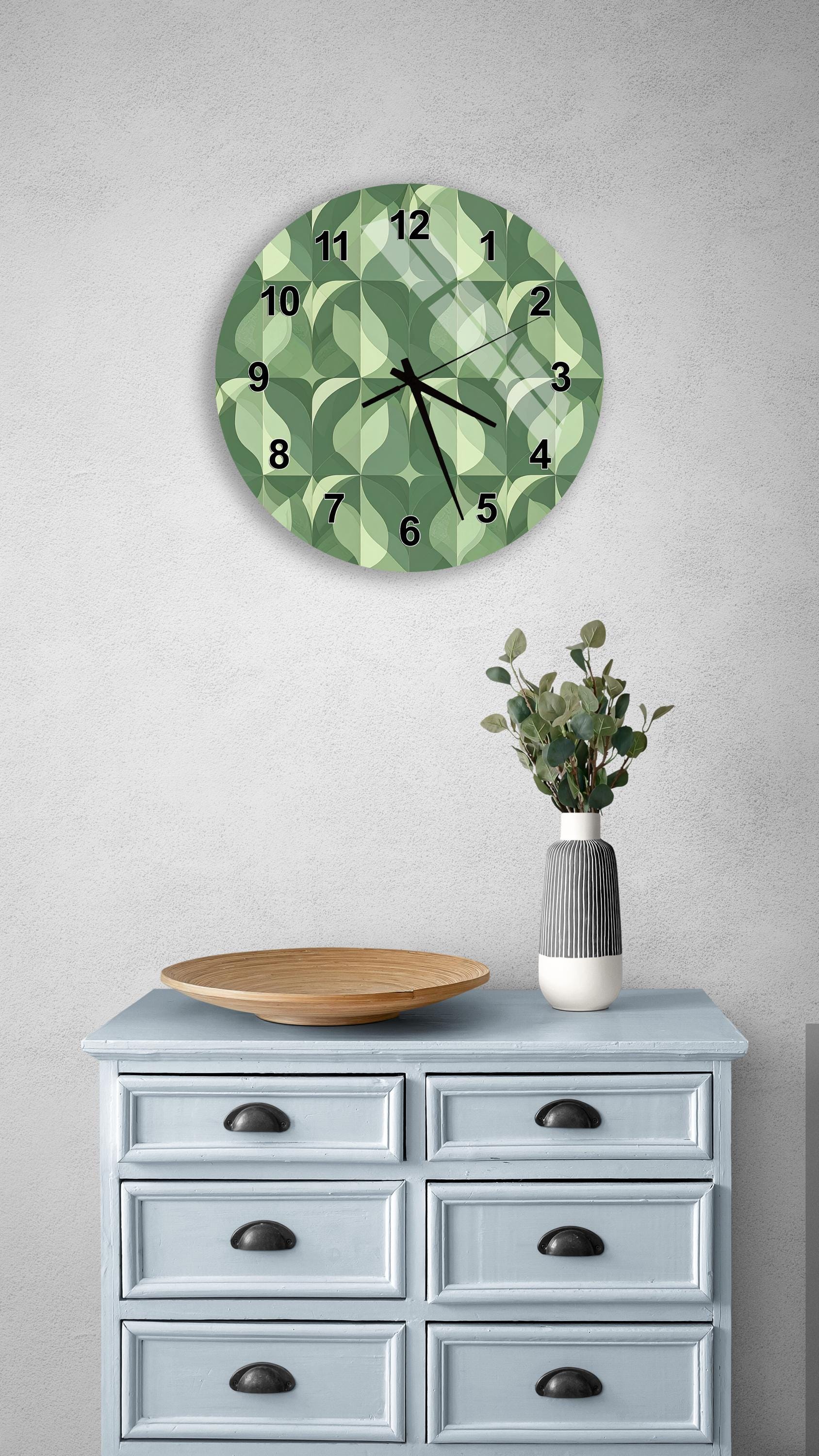 a wall clock with a green and white geometric pattern, a wooden bowl, and a vase with greenery on a light blue dresser.
