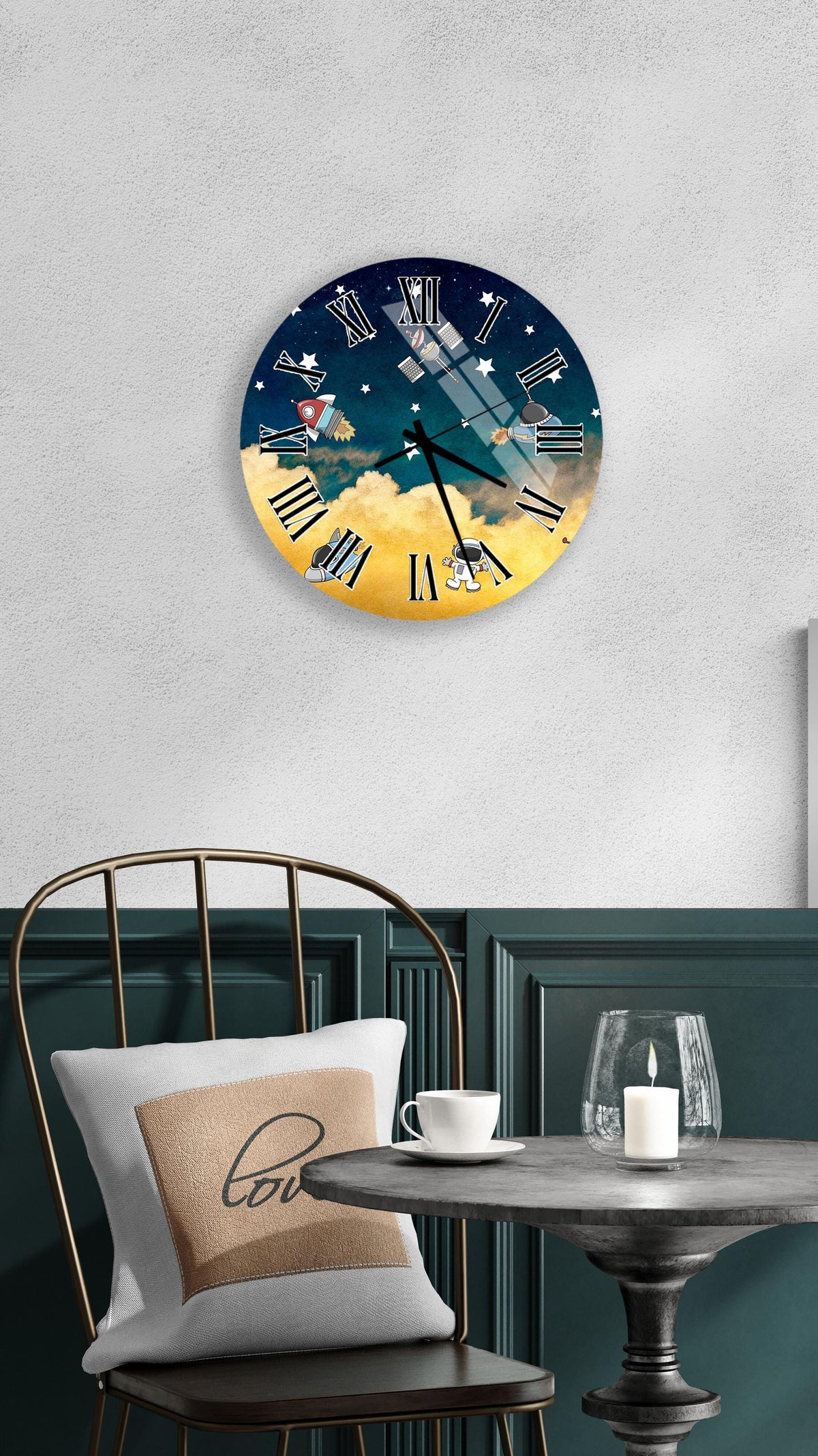 a wall clock with a night sky design, a white table with a candle and a cup, and a chair with a pillow.