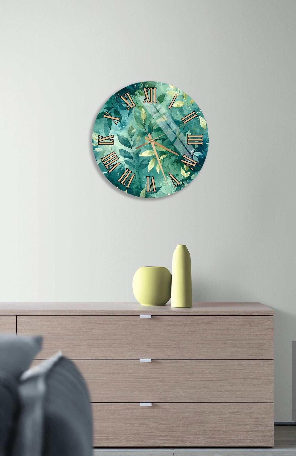 a wall clock with a green and white leaf design, mounted on a wall above a wooden dresser with three drawers.