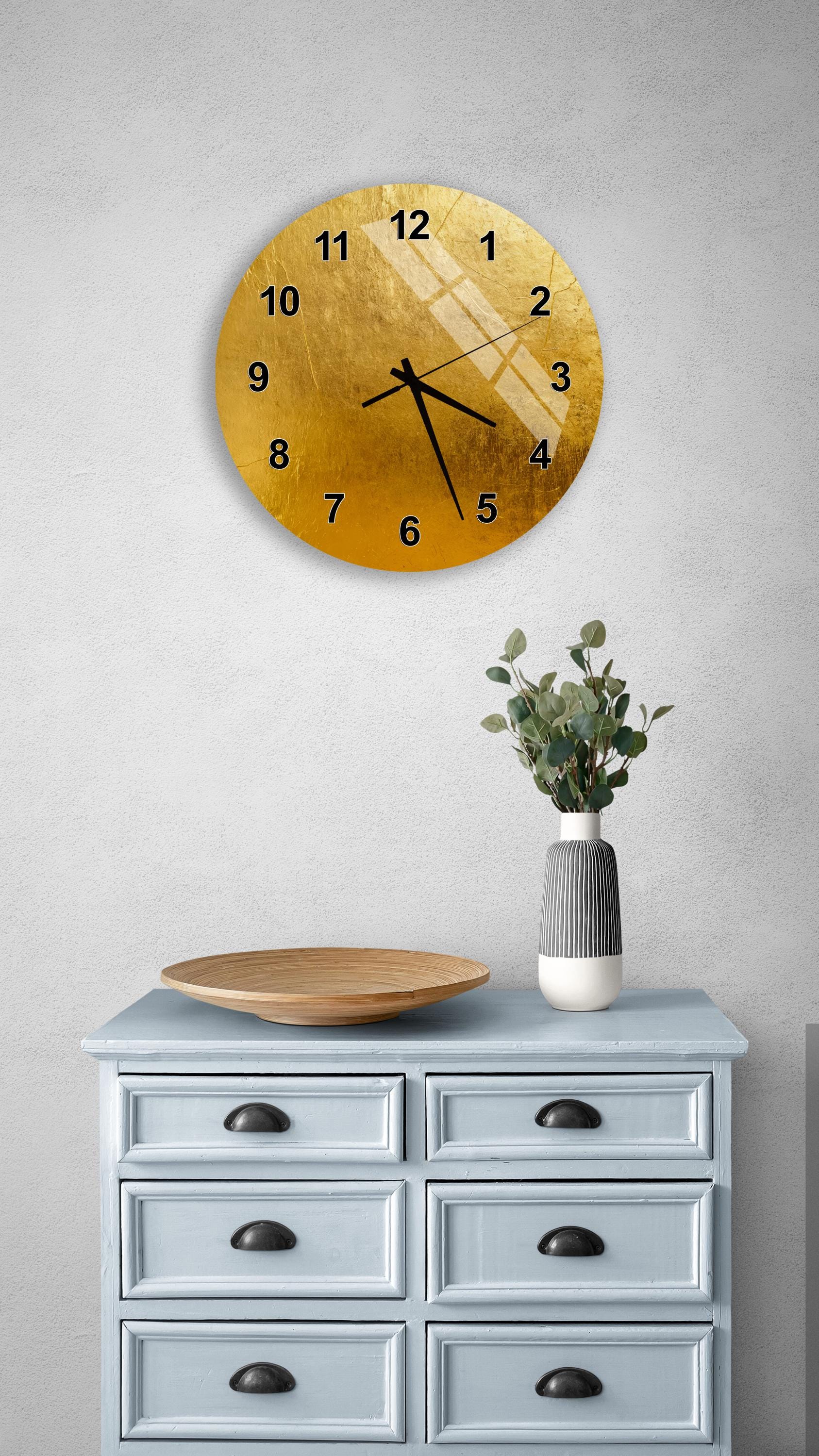 a wall clock with a gold-colored face, a wooden tray, a vase with greenery, and a gray dresser with six drawers.