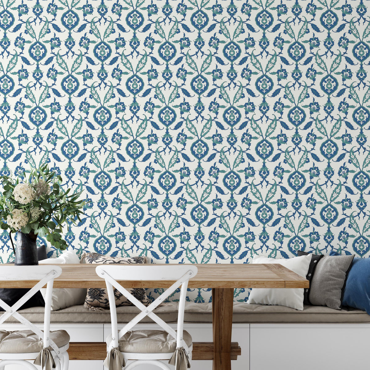 a dining area with a wooden table and white chairs, set against a wall with a blue and white floral pattern wallpaper. A vase of flowers is placed on the table, adding a touch of natural beauty to the scene.