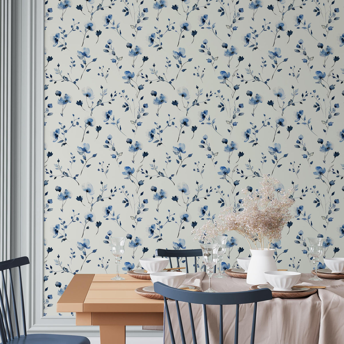 a dining room with a floral wallpaper pattern, a wooden table set with plates, glasses, and a vase of flowers, and a blue chair.