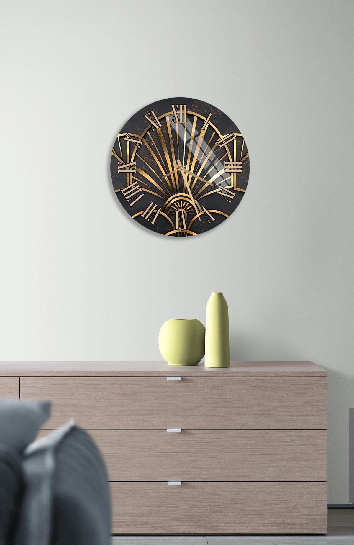 a modern art deco style clock with a black and gold design, mounted on a white wall above a wooden dresser with three drawers.