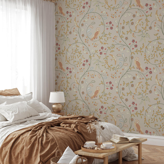 a cozy bedroom with a floral wallpaper, a bed with a brown blanket, and a wooden nightstand with a lamp. There is also a basket of flowers and a book on the nightstand.
