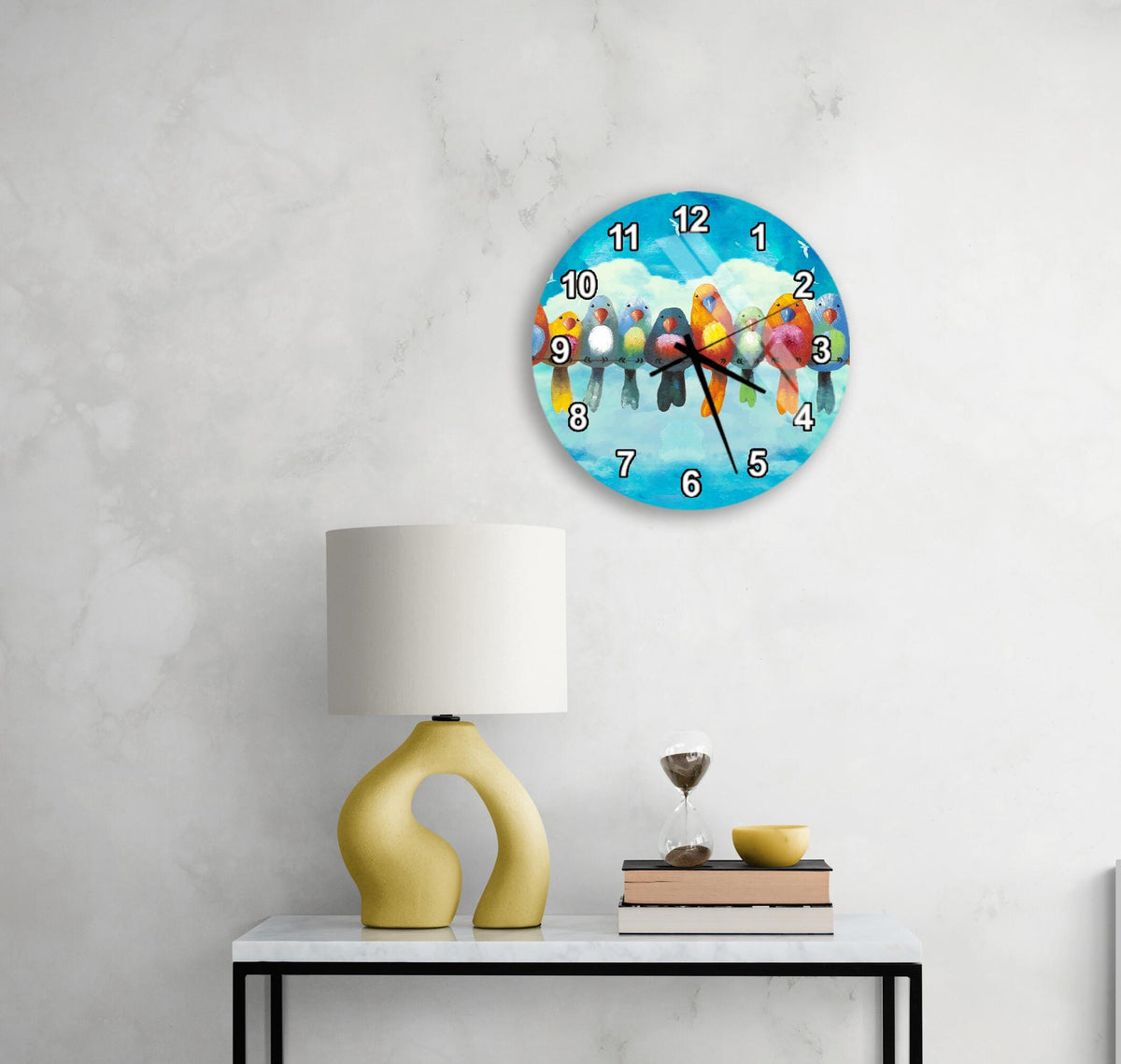 a clock with a bird design on the face, mounted on a wall above a table with a lamp and a small bowl.