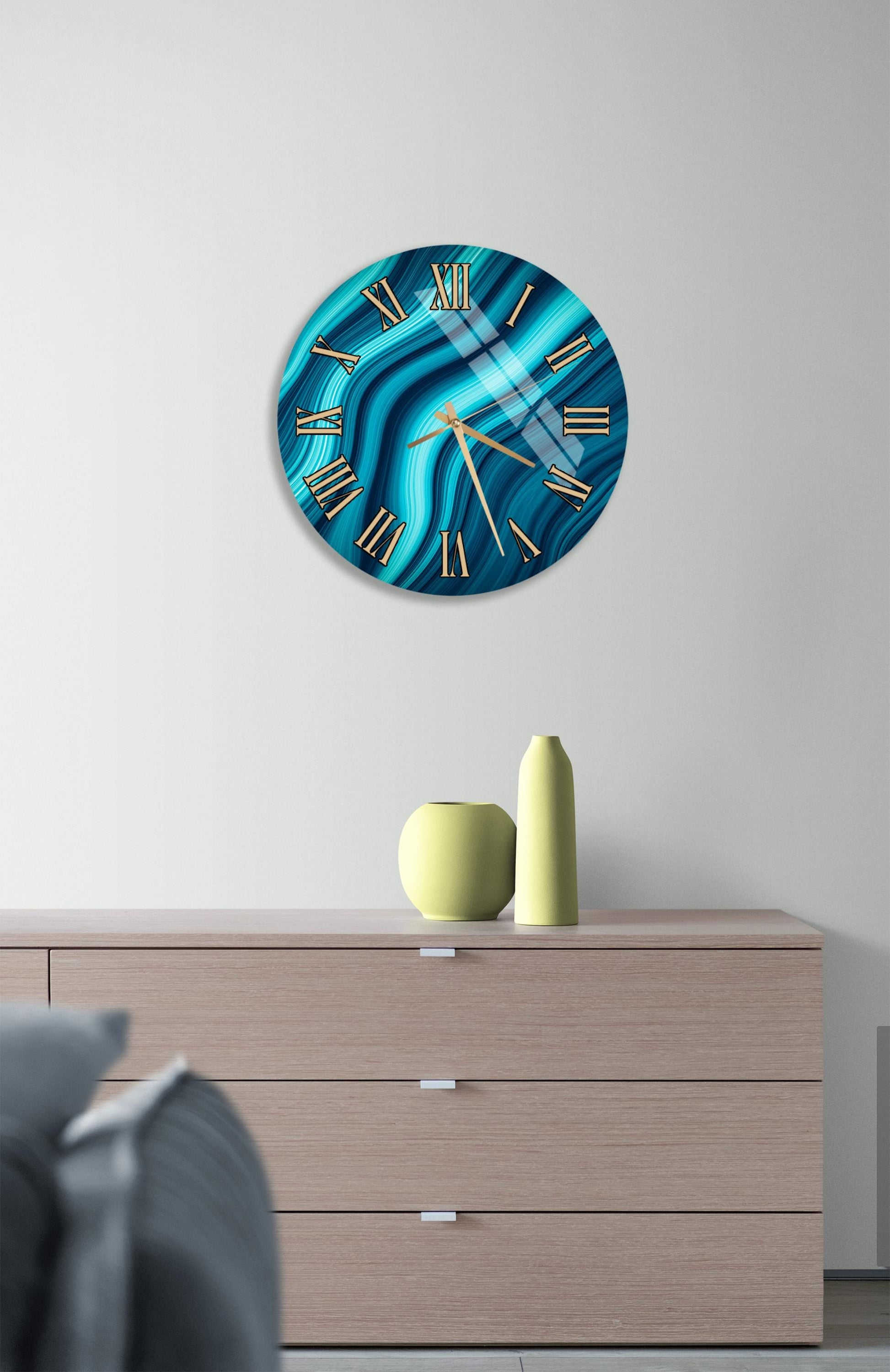 a modern living room with a large, round clock with a blue and white swirl design on the wall above a wooden dresser. The dresser has three drawers and a small vase on top.
