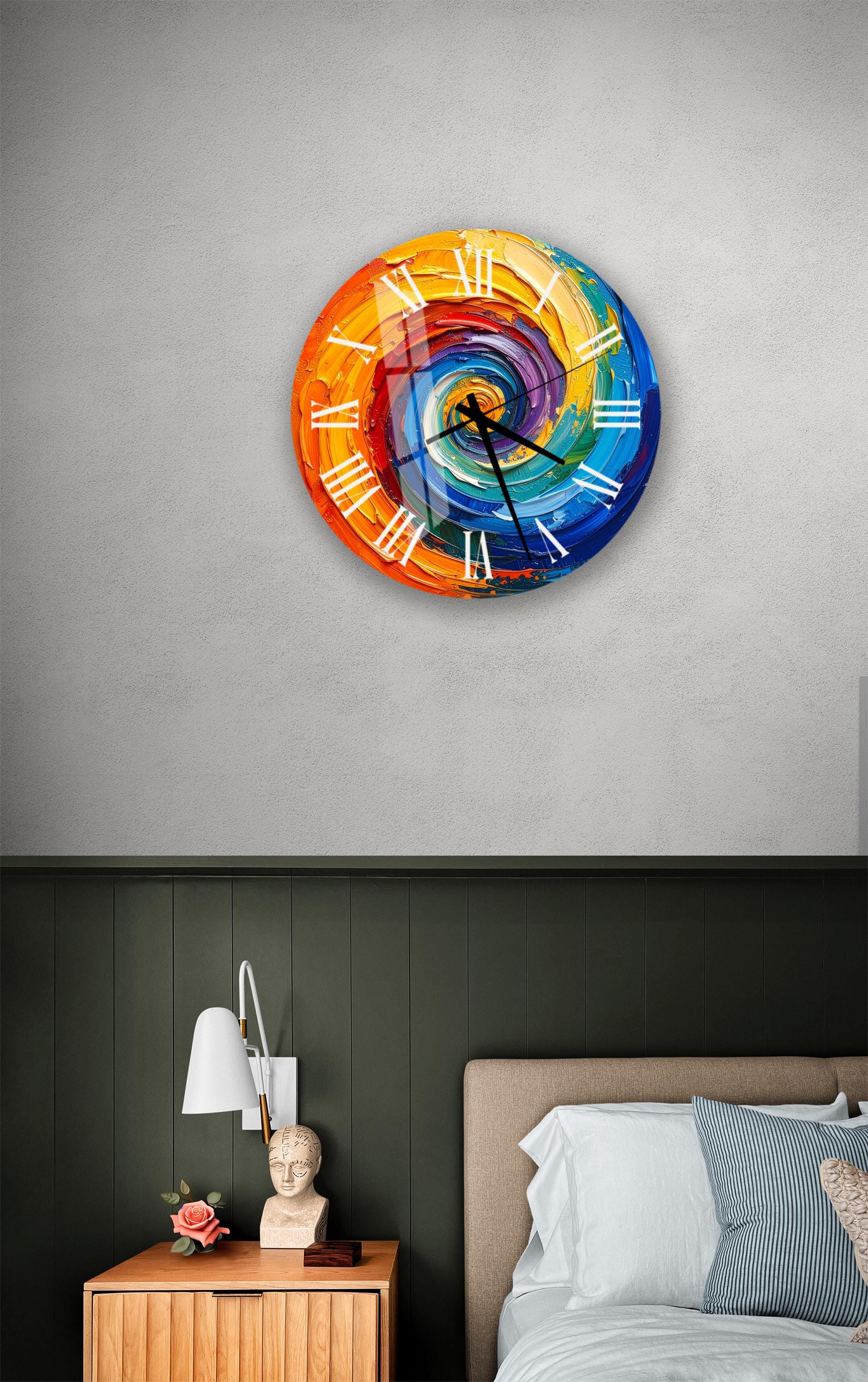 a bedroom setting with a colorful, spiral-patterned wall clock hanging above a bed. The clock has a vibrant design with a mix of orange, blue, green, and purple colors. The room also includes a nightstand with a lamp and a small statue or bust on top.