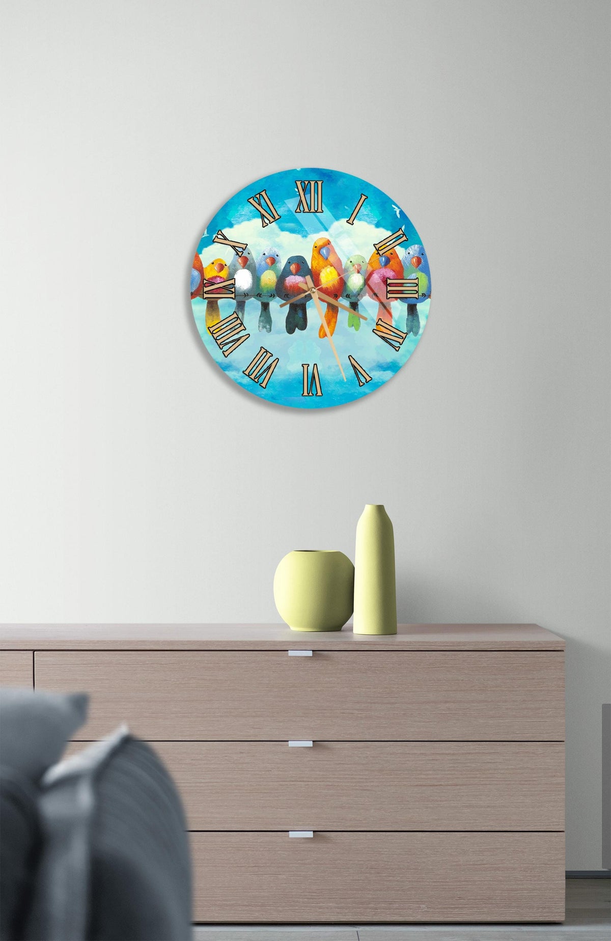 a round clock with a bird design on it, hanging on a wall above a wooden dresser.