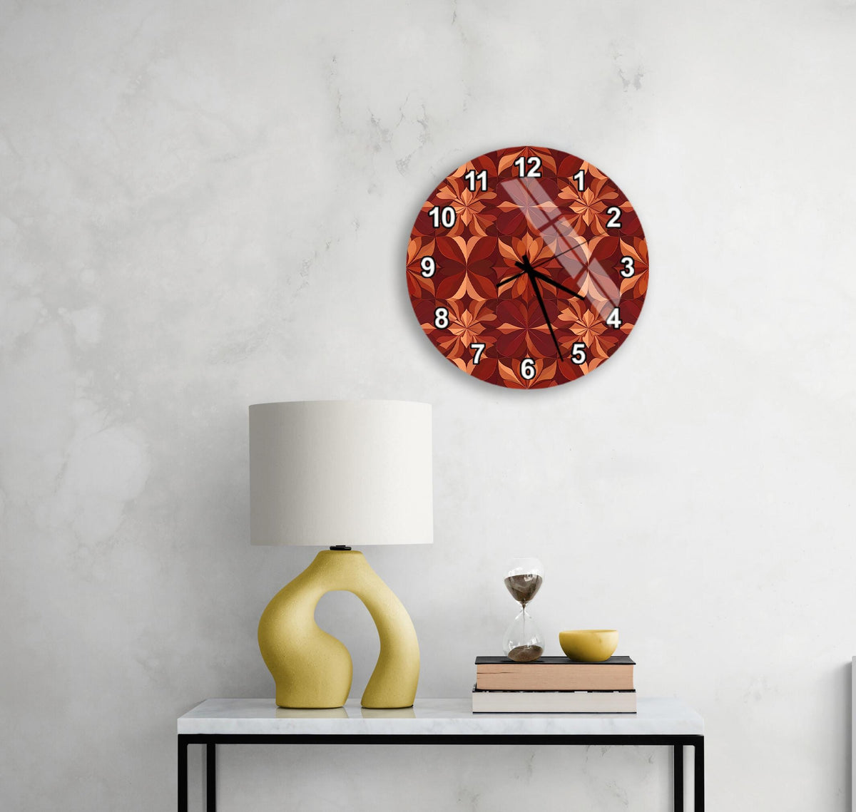 a modern wall clock with a floral design, a yellow lamp on a white table, and a stack of books and a glass of wine on the table.