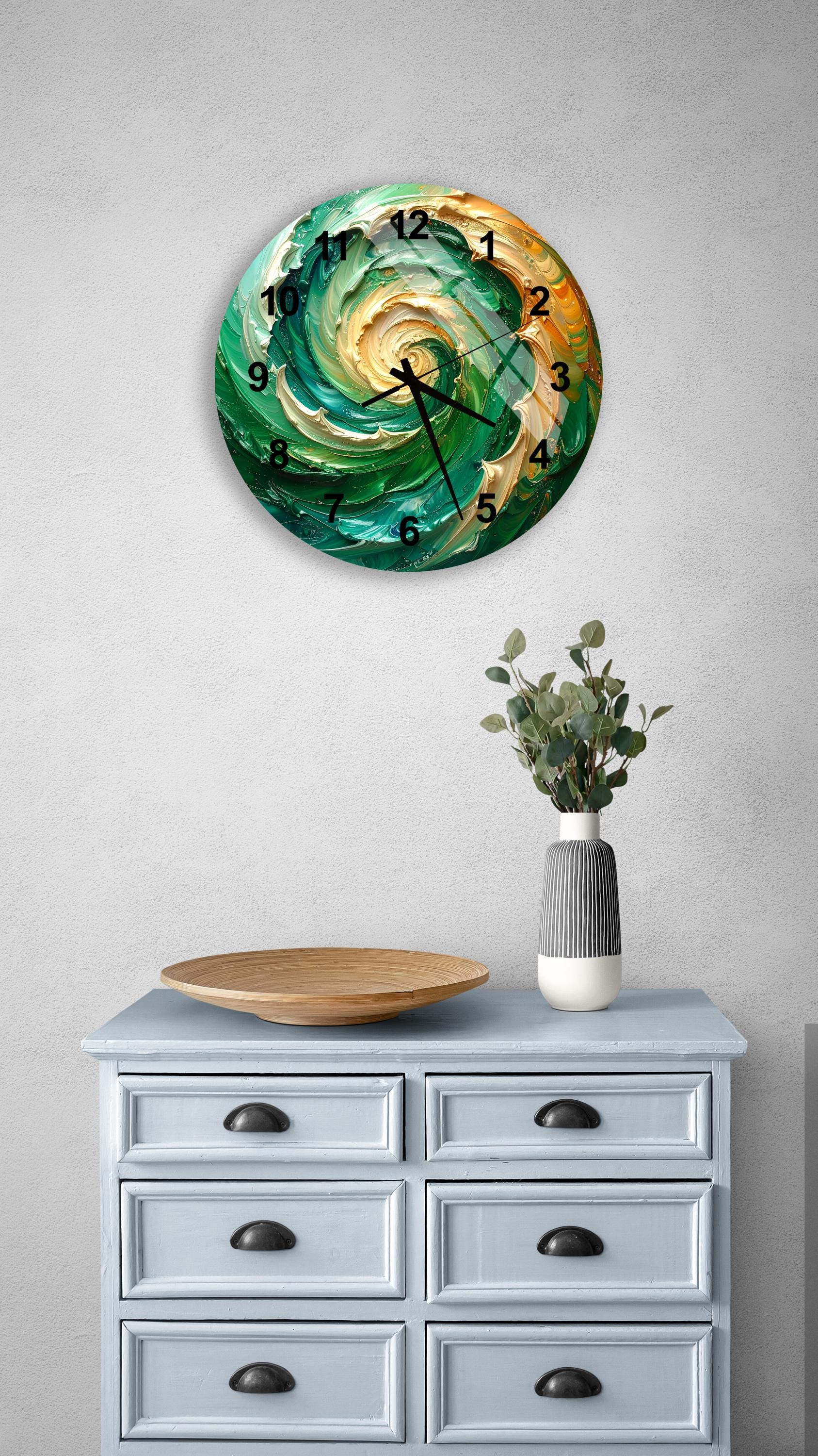 a wall clock with a swirling green and orange design, mounted on a wall above a light blue dresser with six drawers. The dresser also has a vase with greenery and a wooden tray on top.