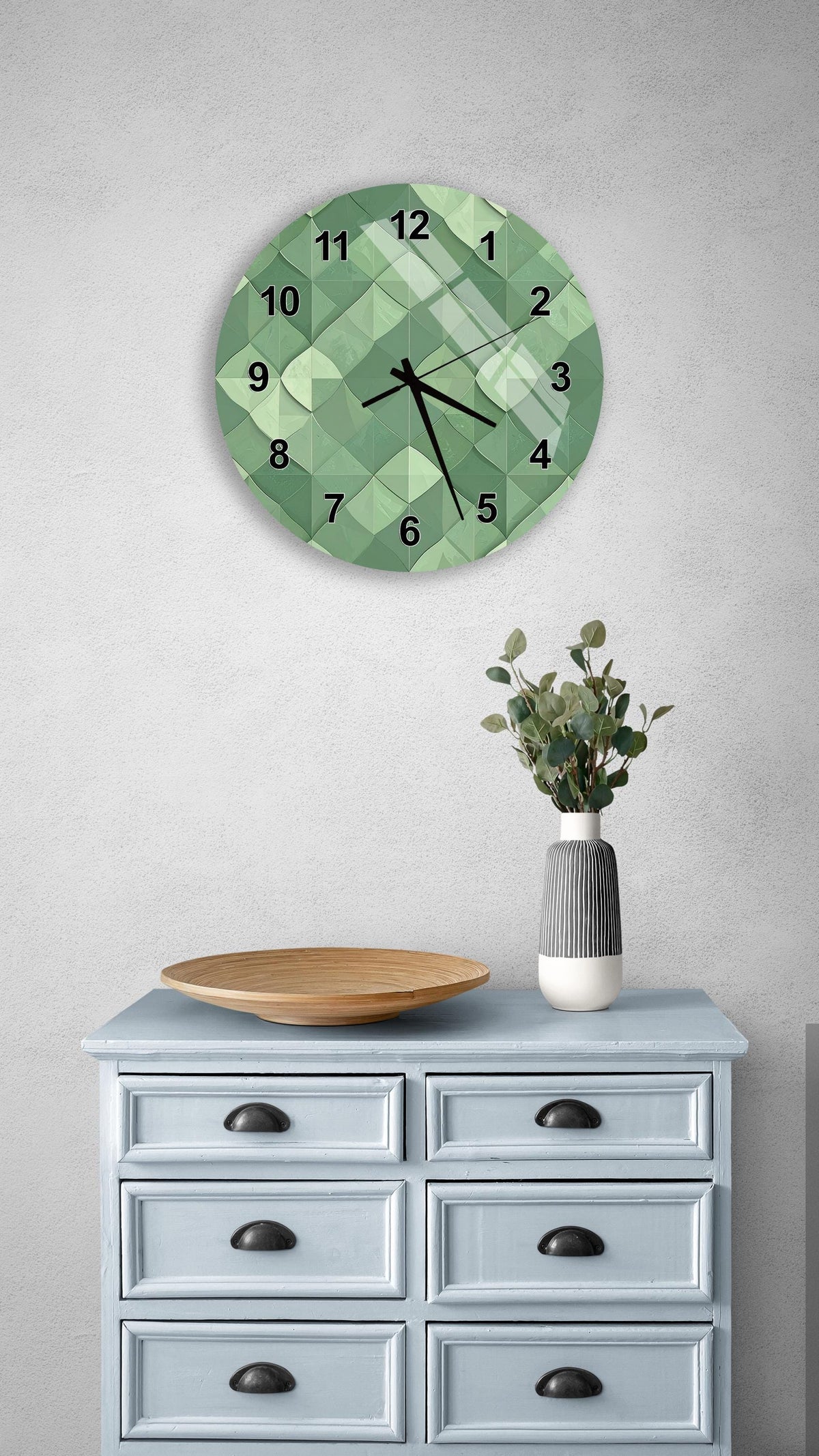 a wall clock with a green geometric design, a wooden bowl on a light blue dresser, and a vase with greenery.