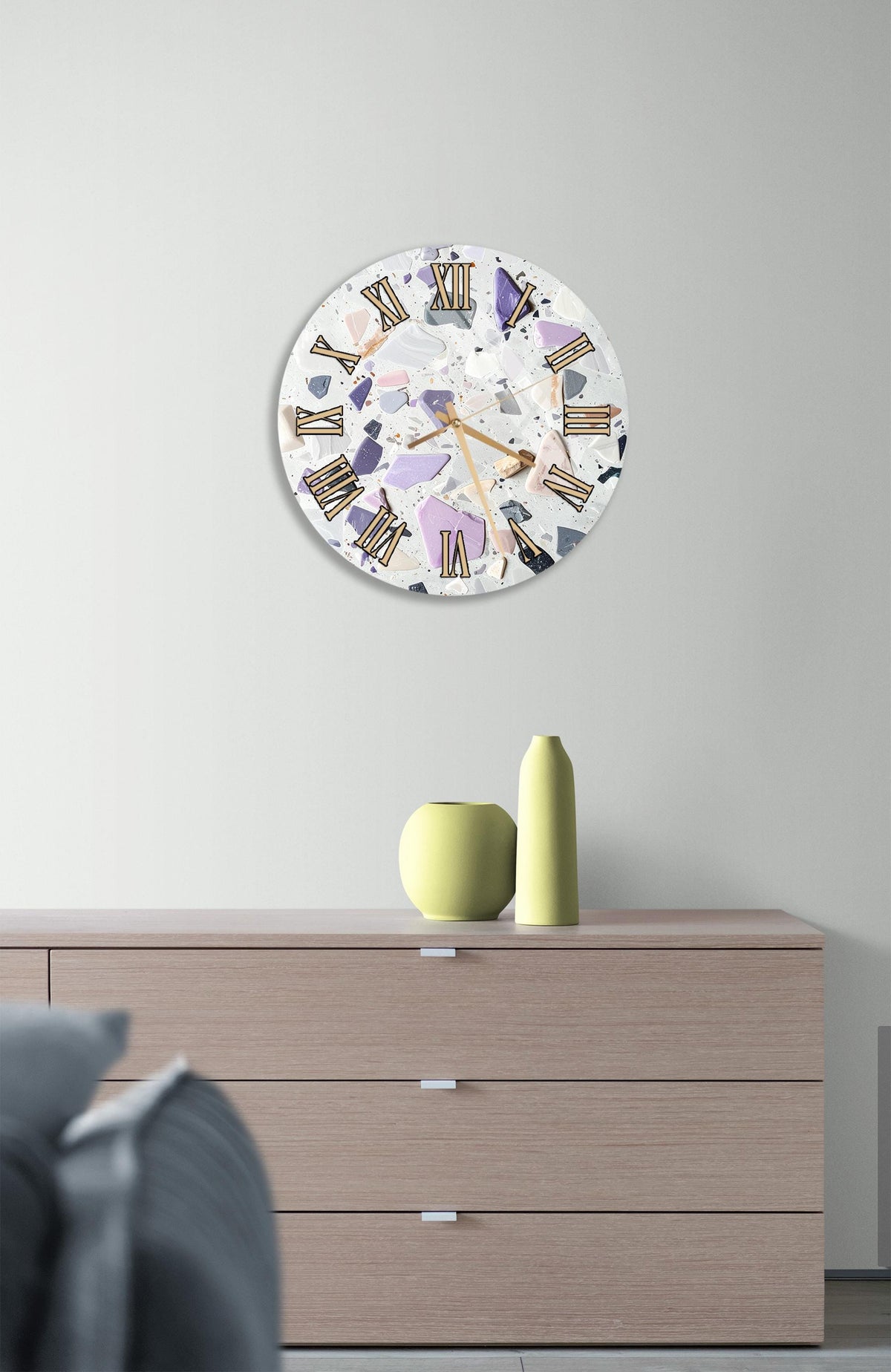 a modern clock with a white face and colorful Roman numerals, mounted on a wall above a wooden dresser.