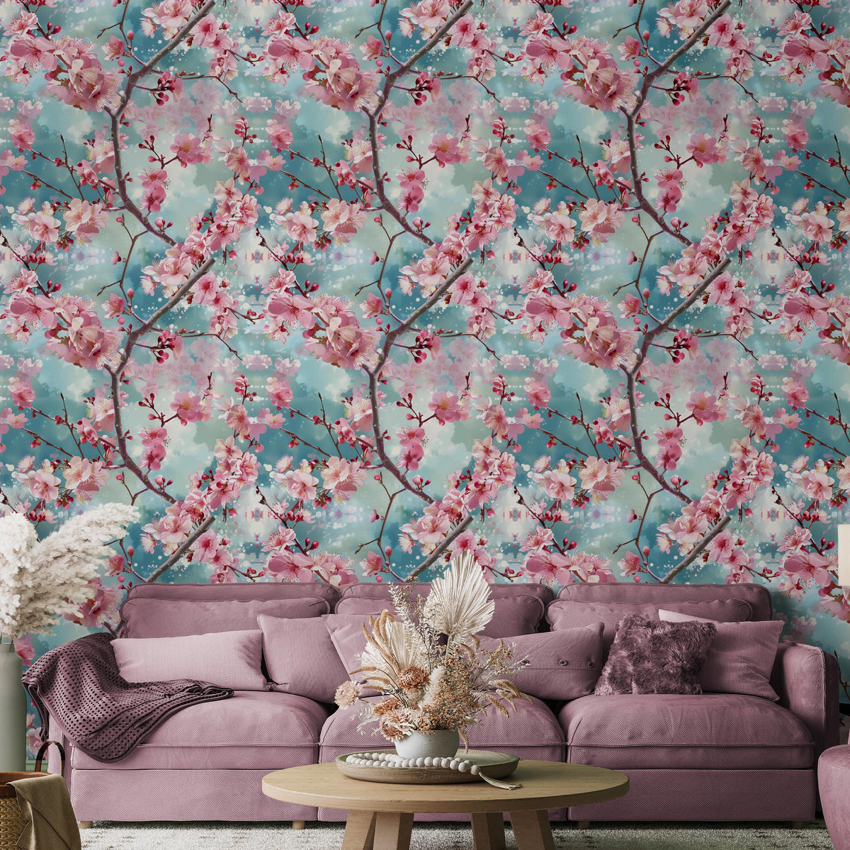 a living room with a large floral wallpaper on the wall behind a pink sofa. The sofa is adorned with a vase of flowers and a decorative throw pillow. The room also includes a coffee table with a bowl and a potted plant.