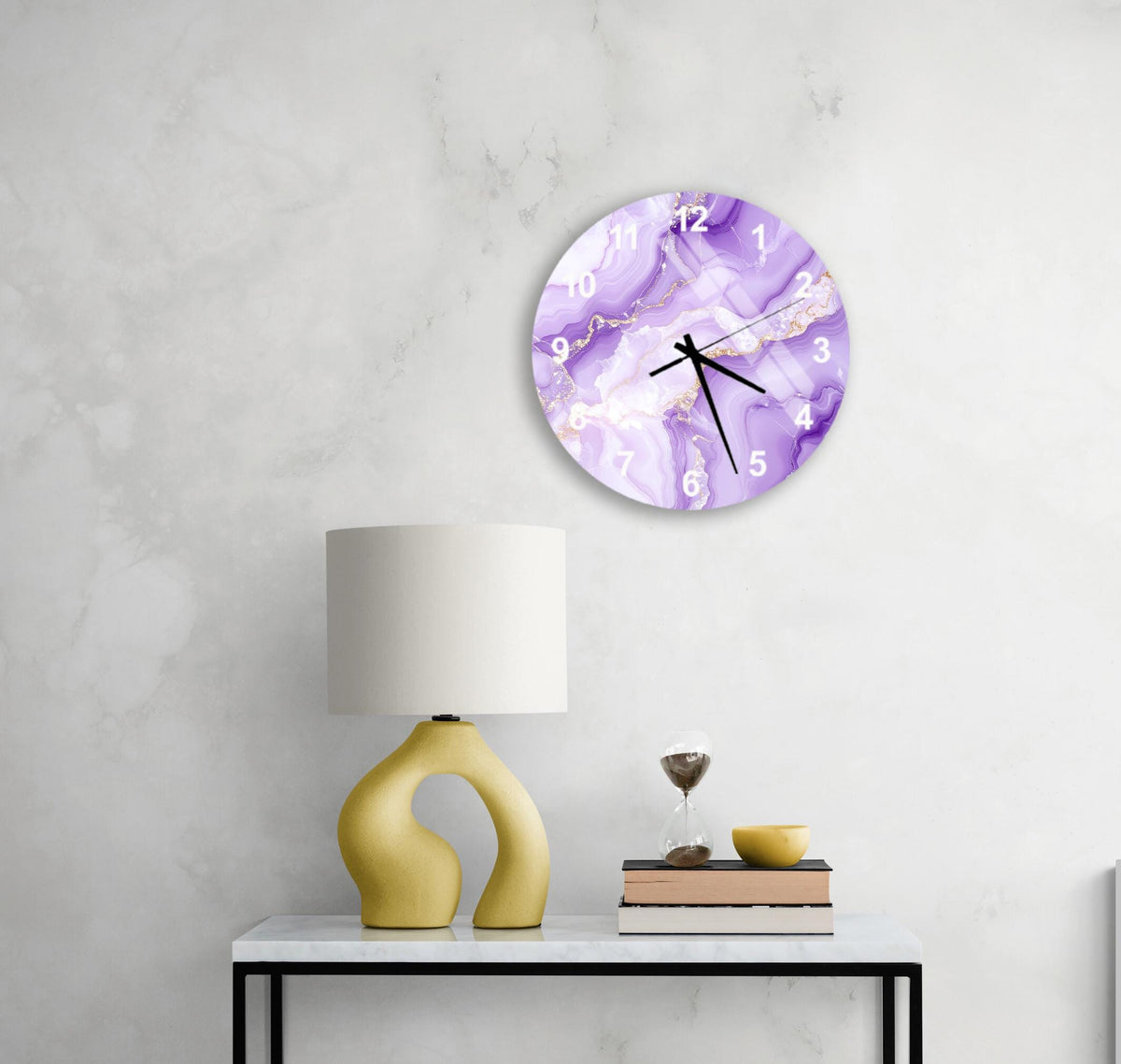 a modern and minimalist interior design with a round clock featuring a purple marble pattern on the wall, a yellow lamp on a white table, and a stack of books and a glass of wine on the table.