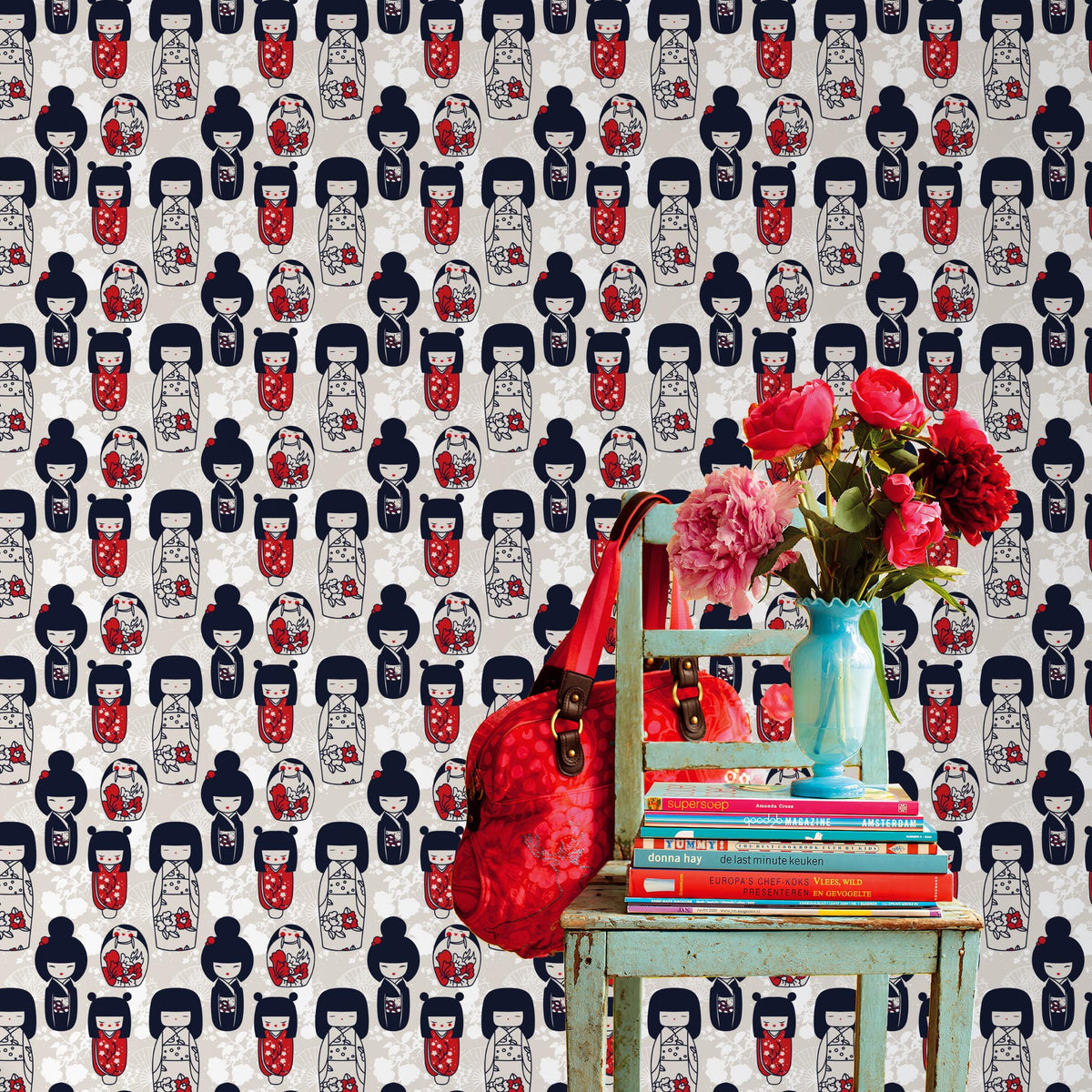 a vibrant scene with a green chair, a stack of books, a red handbag, and a vase of red flowers against a wall with a repeating pattern of Japanese-style dolls.
