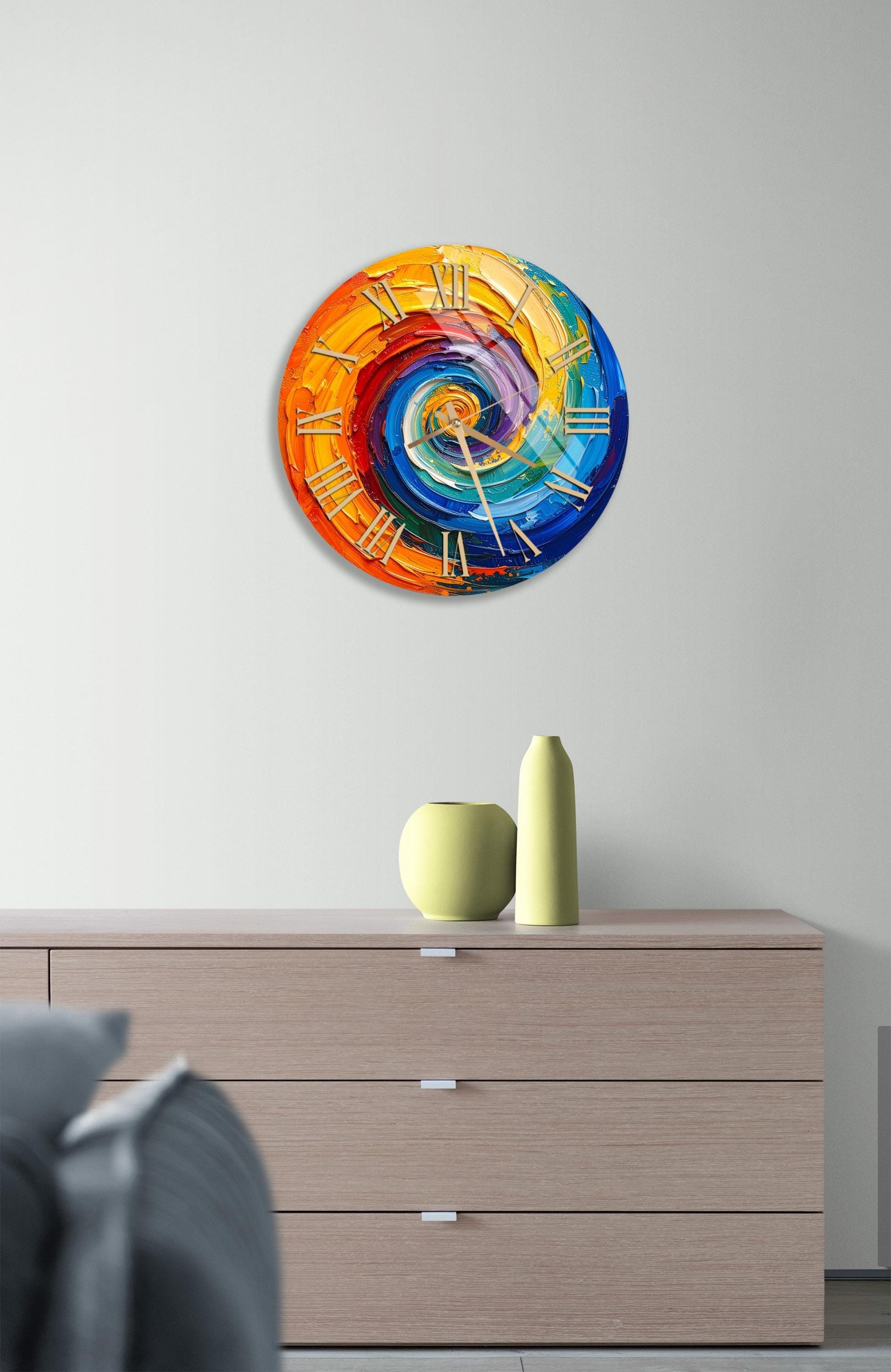 a colorful abstract clock design on a wall, with a wooden dresser below it and a small vase and two vases on top of the dresser.