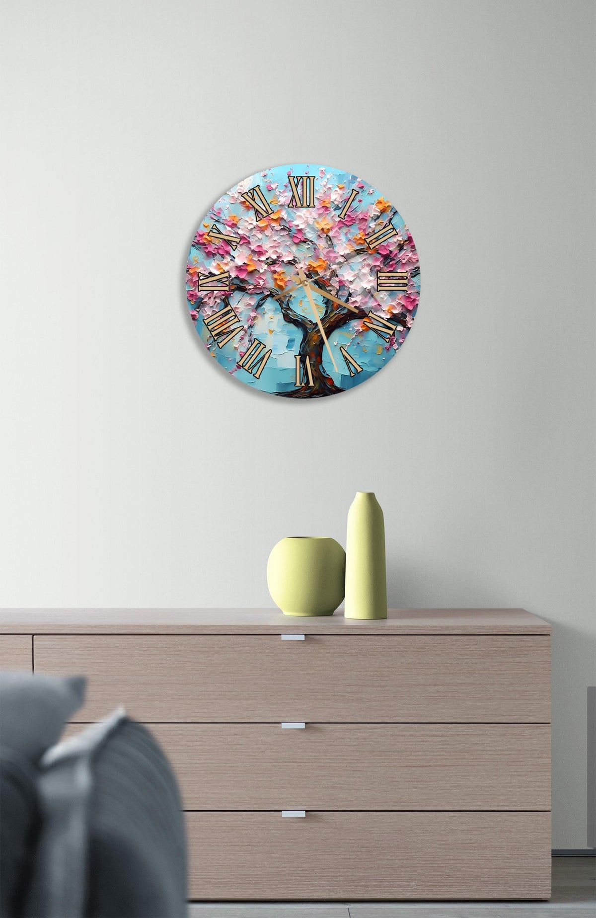 a round clock with a tree design on it, mounted on a wall above a wooden dresser.