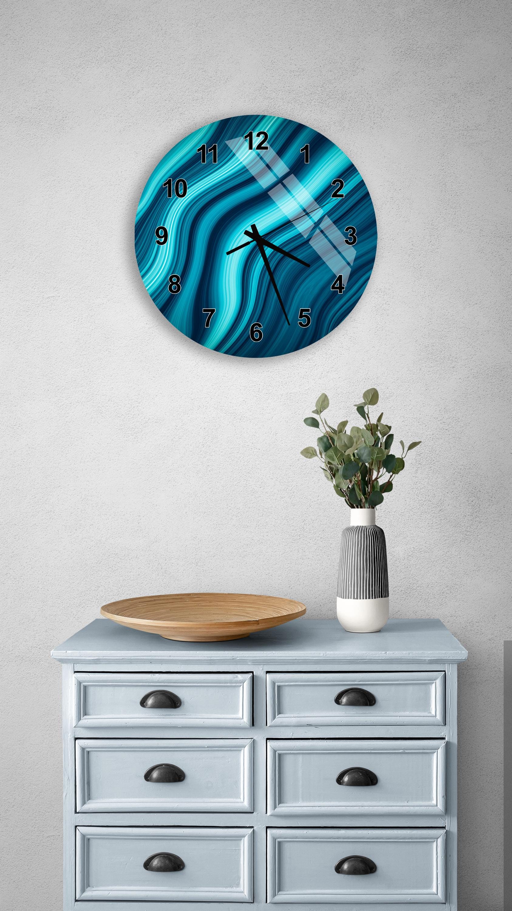 a blue and white clock with a unique wave pattern on its face, mounted on a wall above a light blue dresser with six drawers. The dresser also has a vase of greenery and a wooden tray on top.