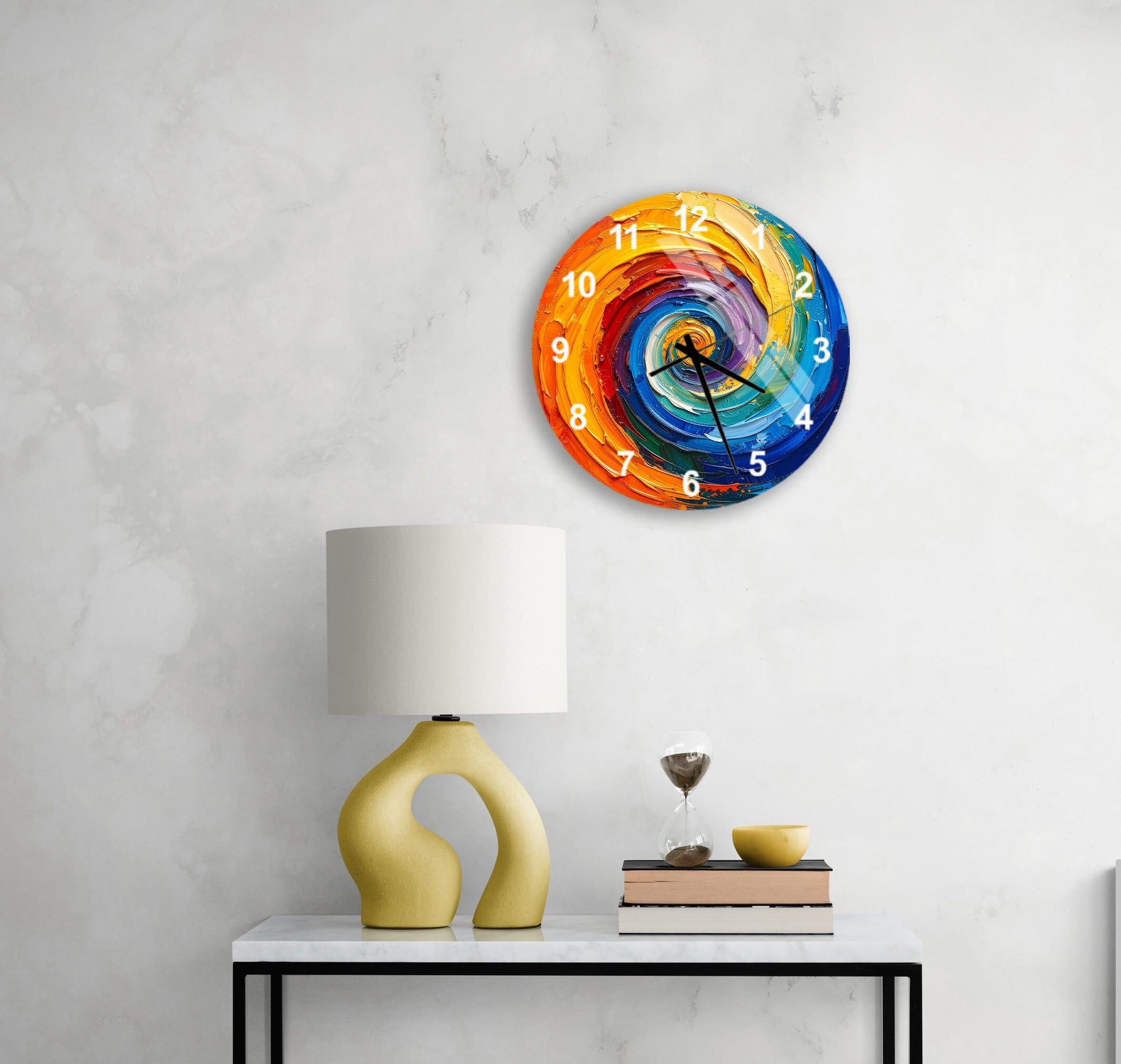 a colorful, abstract clock with a spiral design on a white wall, accompanied by a yellow lamp, a stack of books, and a glass of water on a white table.