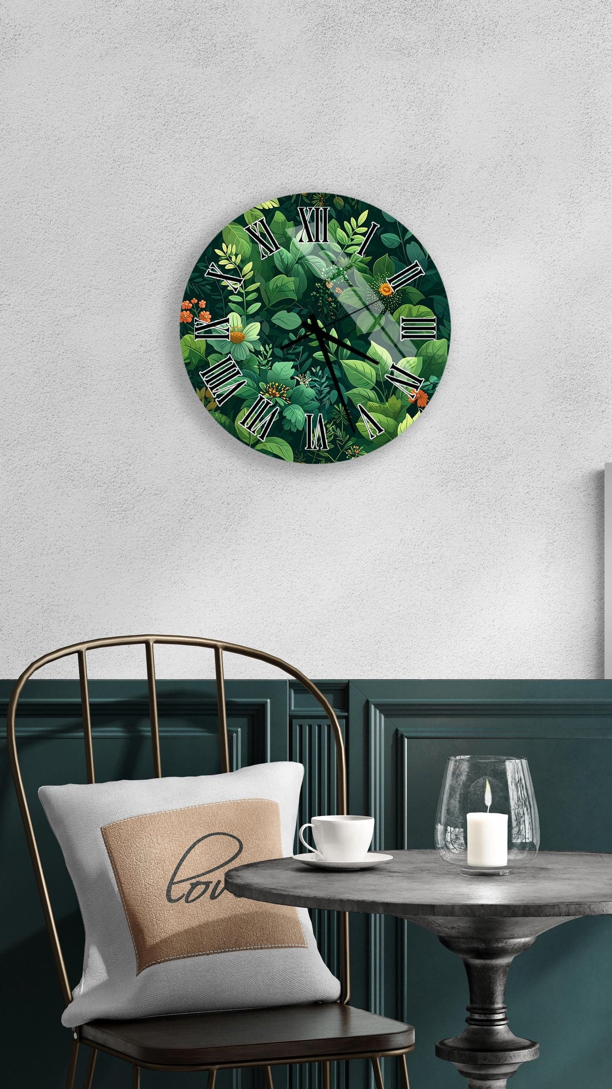 a round wall clock with a green and leafy design, mounted on a white wall above a table with a white tablecloth. The table has a white cup and a candle on it, creating a cozy and inviting atmosphere.