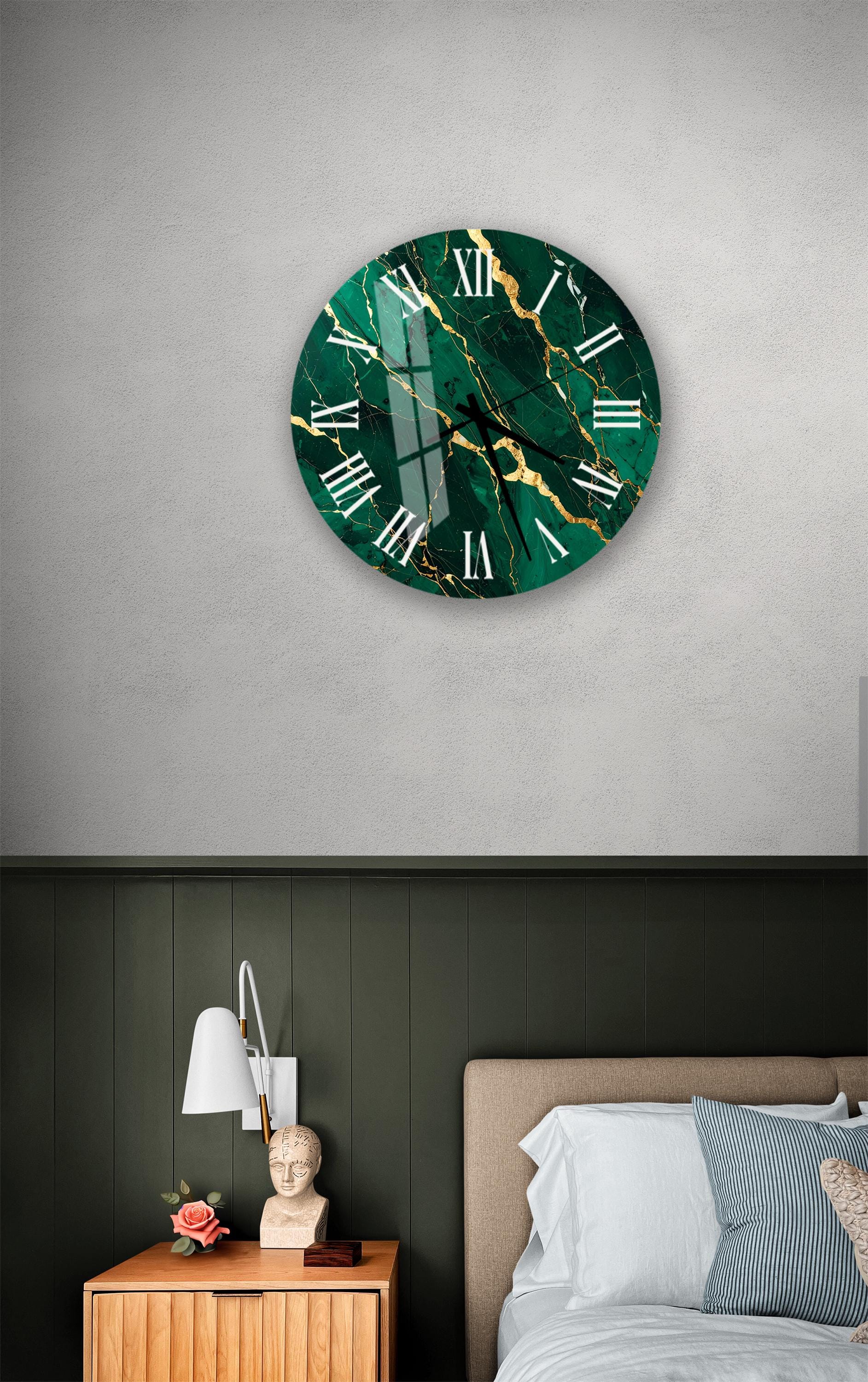 a bedroom setting with a large green marble clock hanging on the wall above a bed. The clock has a unique design with a green and gold color scheme and a cracked marble texture. The room also includes a nightstand with a lamp and a small statue, creating a cozy and stylish atmosphere.