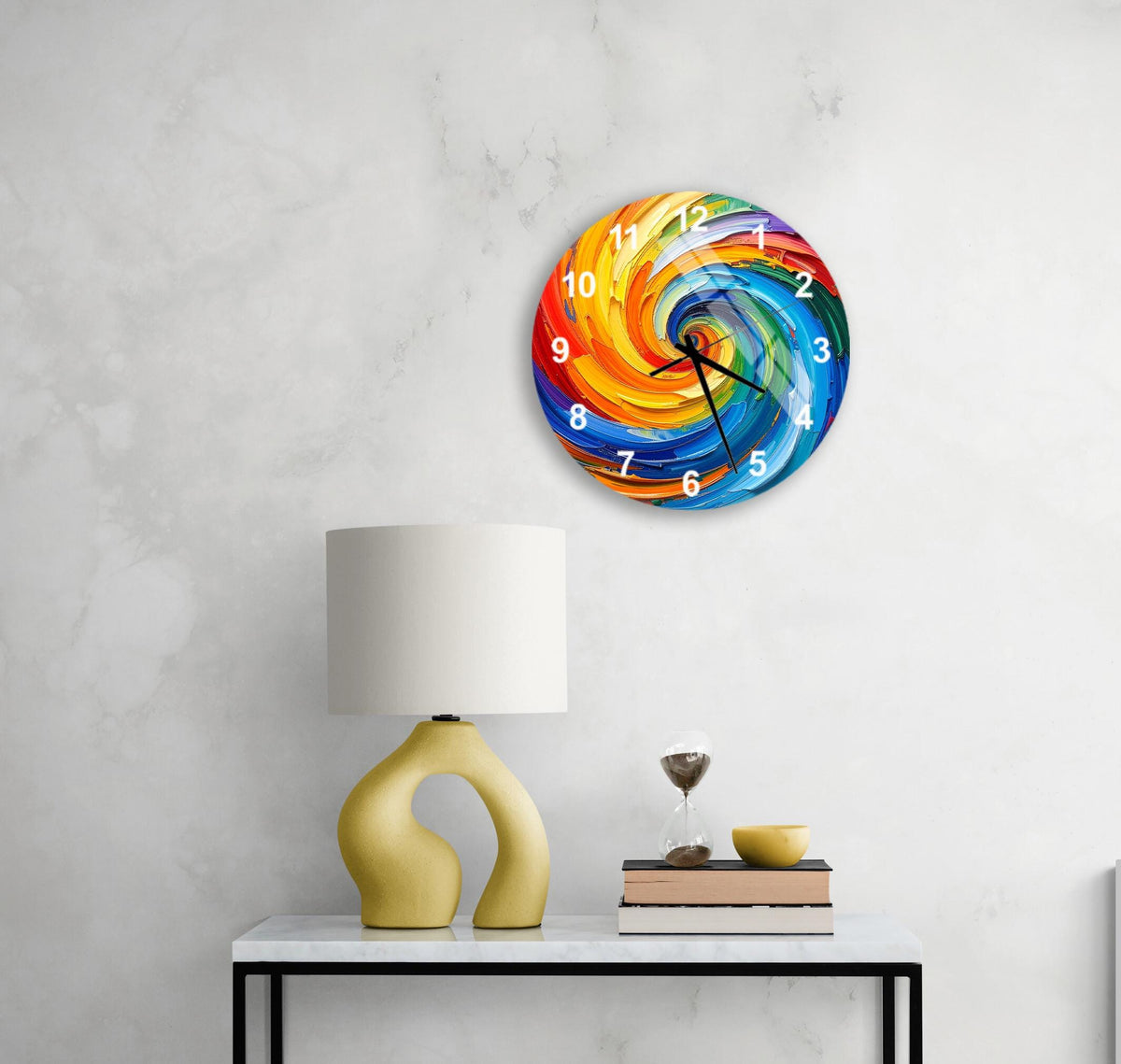 a colorful, abstract clock with swirling patterns on its face, mounted on a wall above a white table with a yellow lamp and a stack of books.