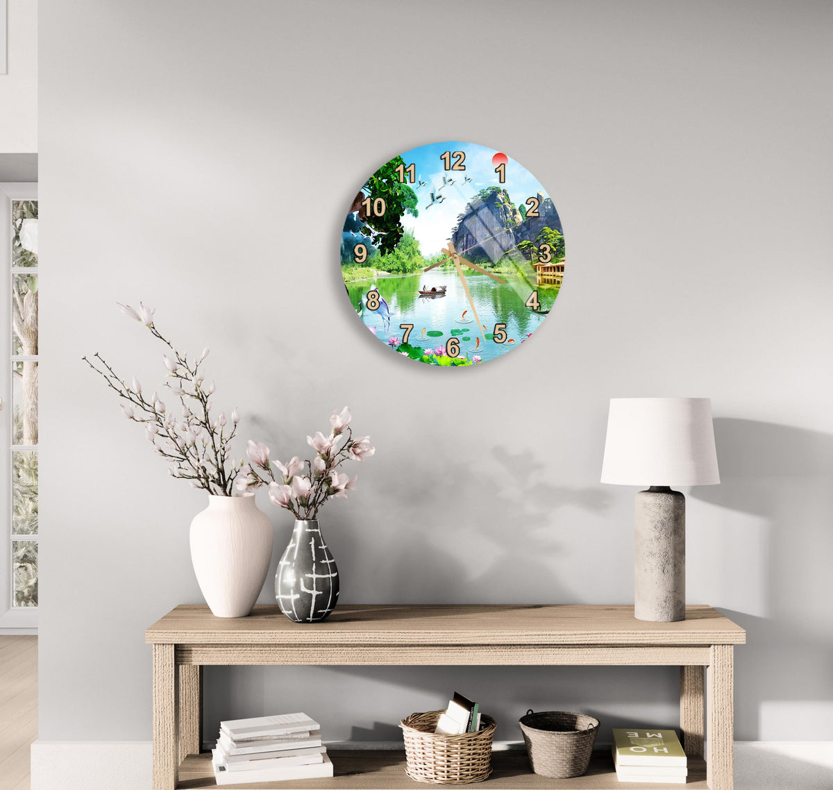 a wall clock with a scenic outdoor view, a wooden table with a lamp, a vase with flowers, and some books on a shelf.