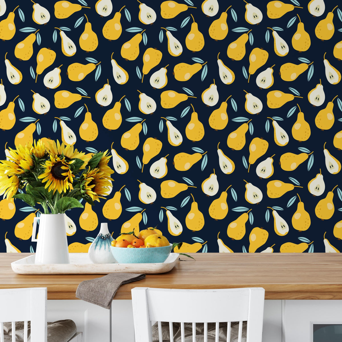a dining table with a vase of sunflowers, a bowl of fruit, and a white chair. The table is set against a wall with a repeating pattern of yellow and green pears.