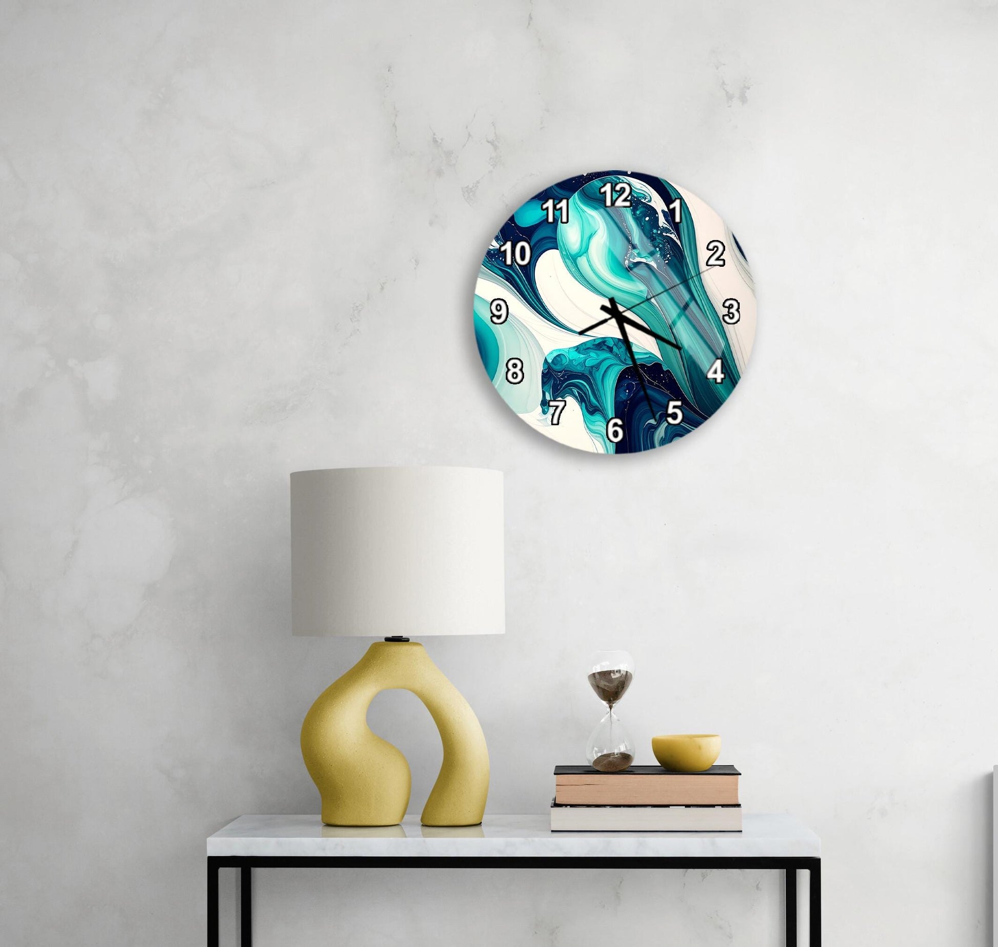 a modern, abstract wall clock with a blue and white color scheme, mounted on a white wall above a white table with a yellow lamp and a stack of books.
