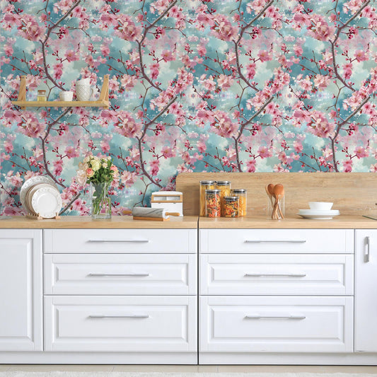 a kitchen counter with white cabinets and drawers, adorned with various kitchen items such as a vase of flowers, a bowl, and a stack of books. The wall behind the counter is decorated with a floral wallpaper, adding a touch of nature and color to the space.