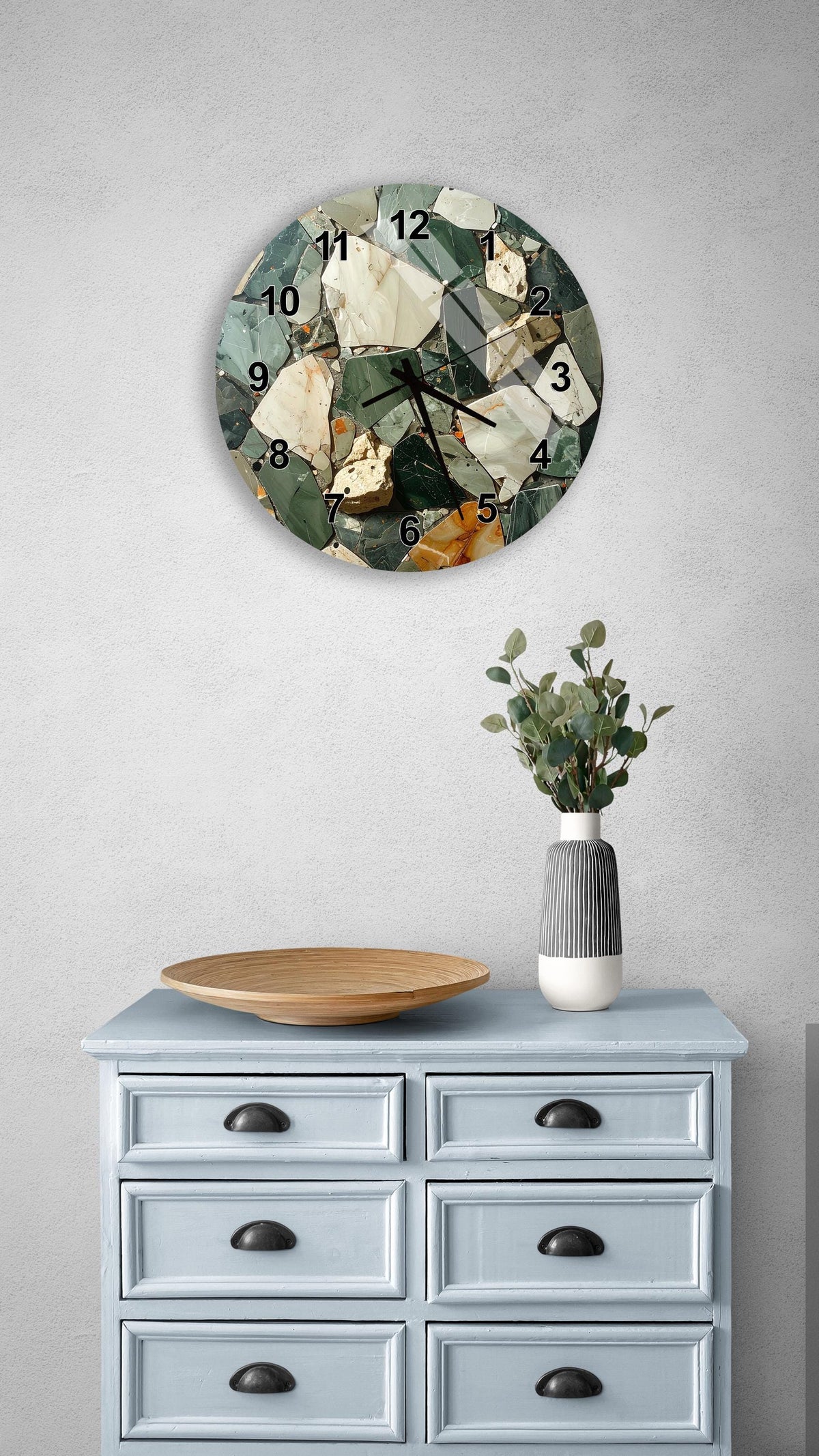 a wall clock with a mosaic design, a wooden tray, a vase with greenery, and a light blue dresser with six drawers.