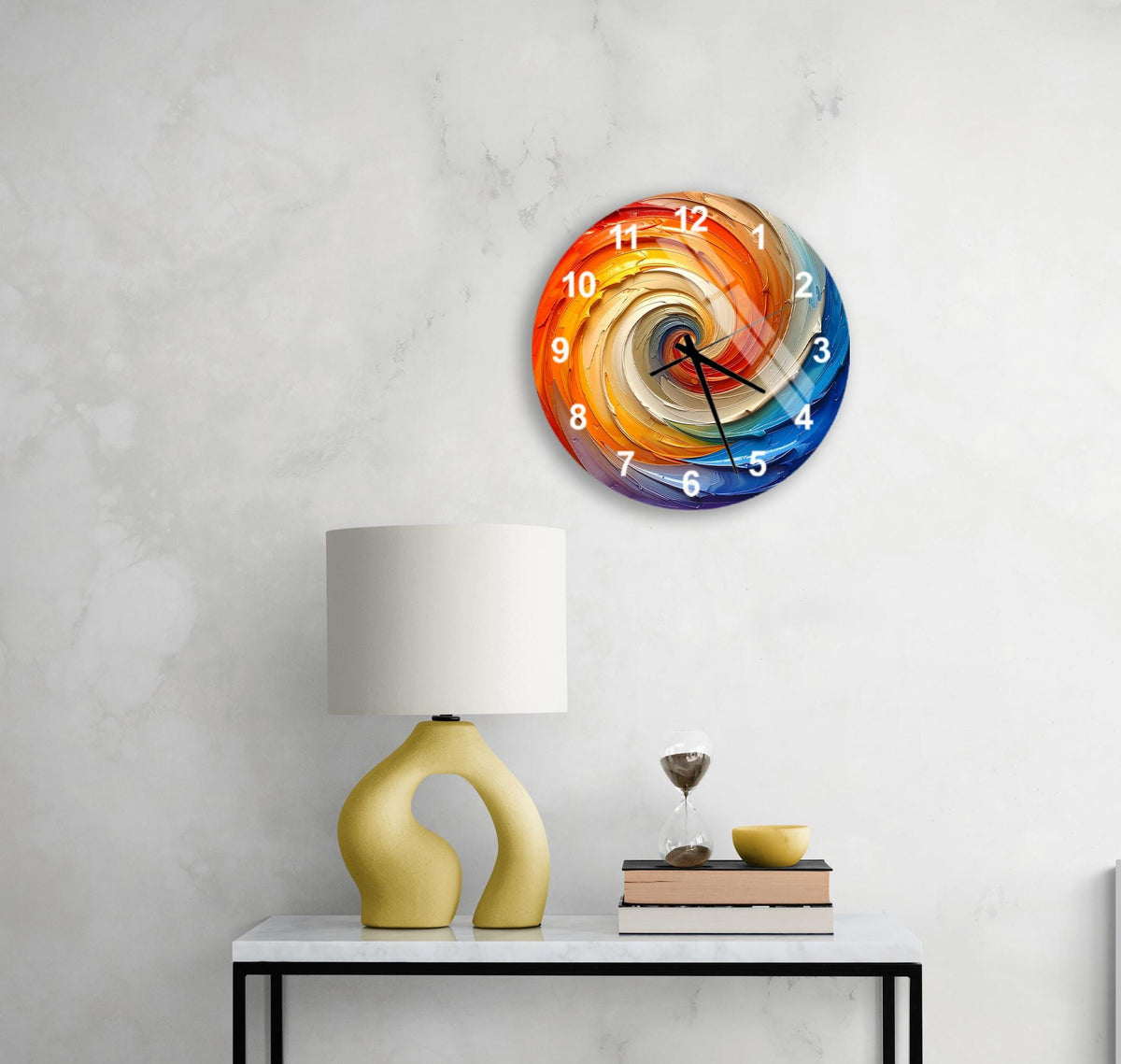 a colorful, spiral-patterned wall clock hanging on a white wall above a white table with a yellow lamp and a stack of books.