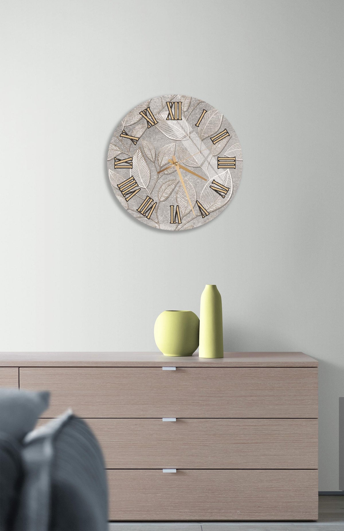 a modern living room with a large wall clock displaying Roman numerals, a wooden dresser with a vase and a small green sculpture, and a gray couch in the background.