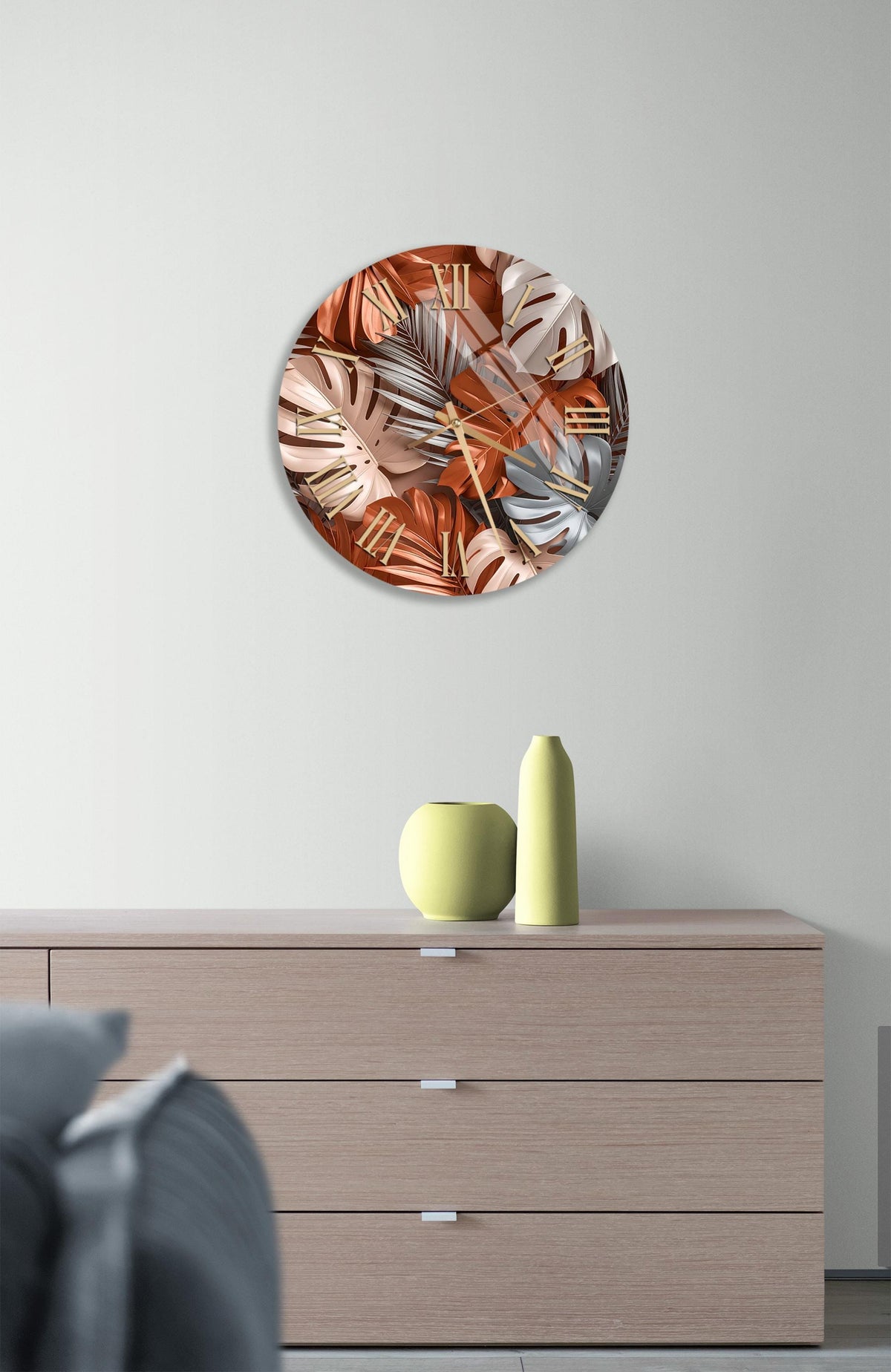 a round wall art piece with a vibrant design of orange and pink leaves, hanging above a wooden dresser with a yellow vase and a gray vase on top.