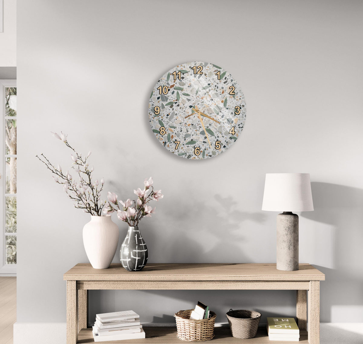 a modern and minimalist living room with a wooden console table, a round wall clock, and various decorative elements such as a vase with flowers, a lamp, and a stack of books.